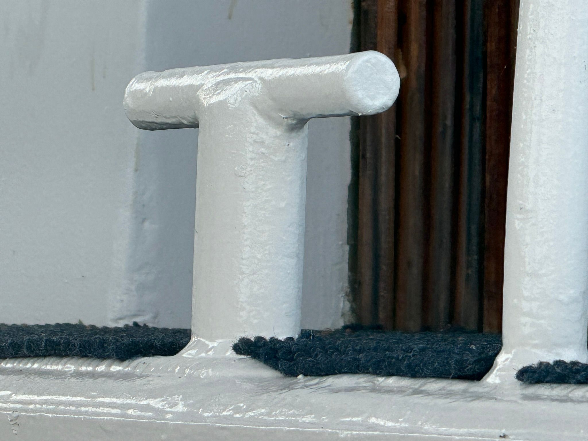 Close-up of a white bollard on a boat with dark carpeting.