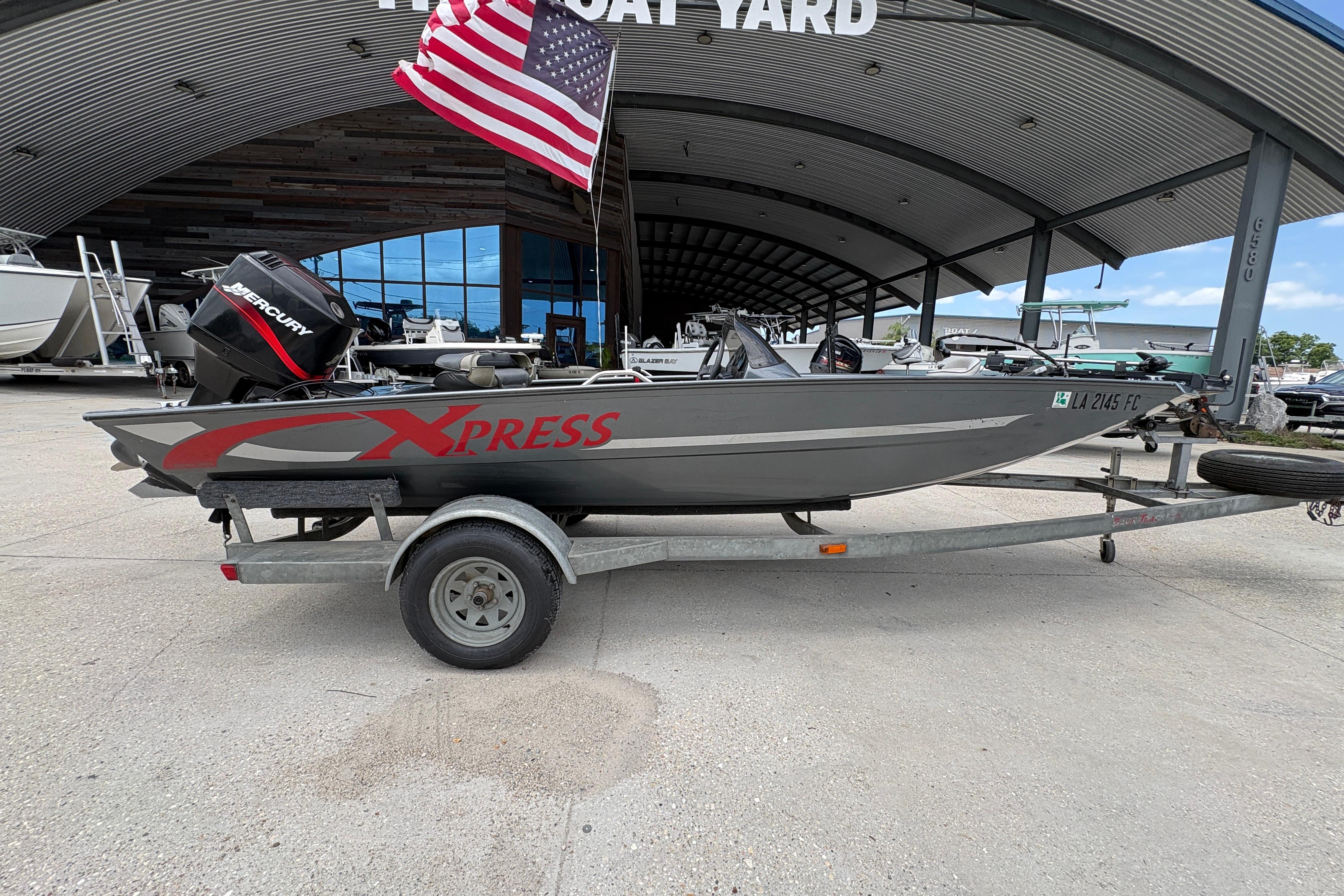 2000 Xpress X18 boat on trailer with American flag, parked at boatyard.