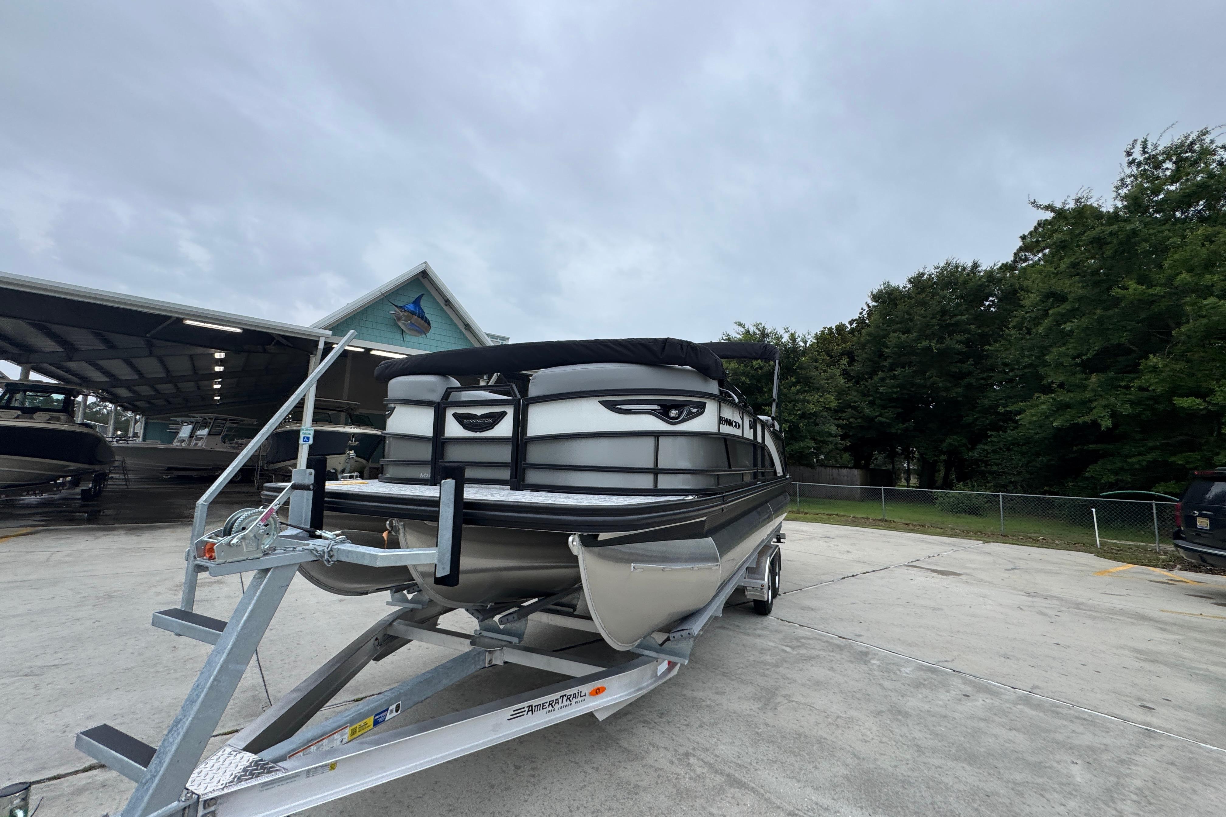 2027 Bennington 24 MFB pontoon boat on trailer, parked outdoors near trees.
