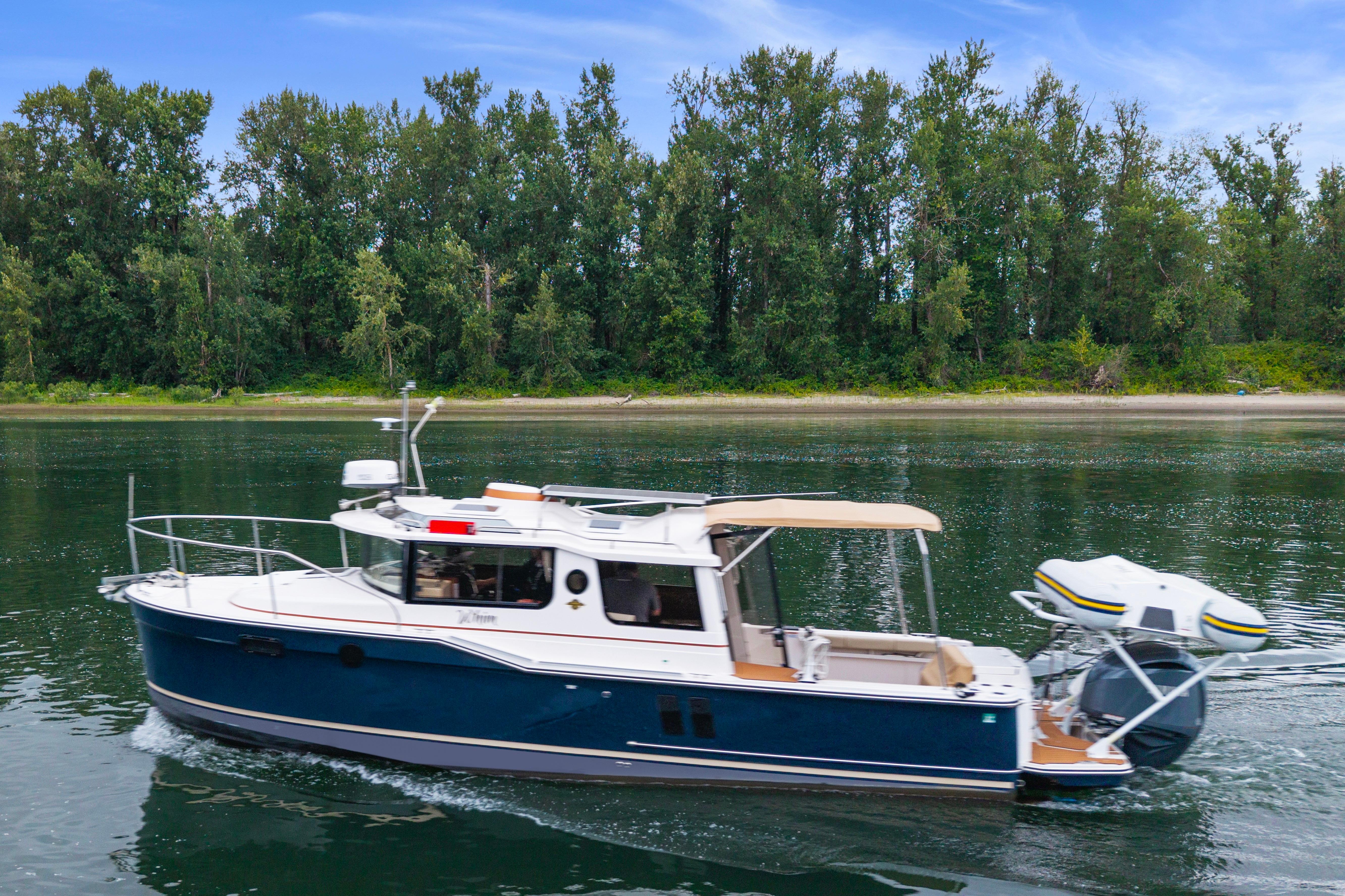 2022 Ranger Tugs R-27 cruising on a serene river with lush green trees.