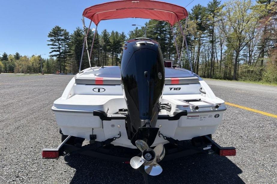 2026 Tahoe T18 boat with outboard motor and red canopy, parked on asphalt.