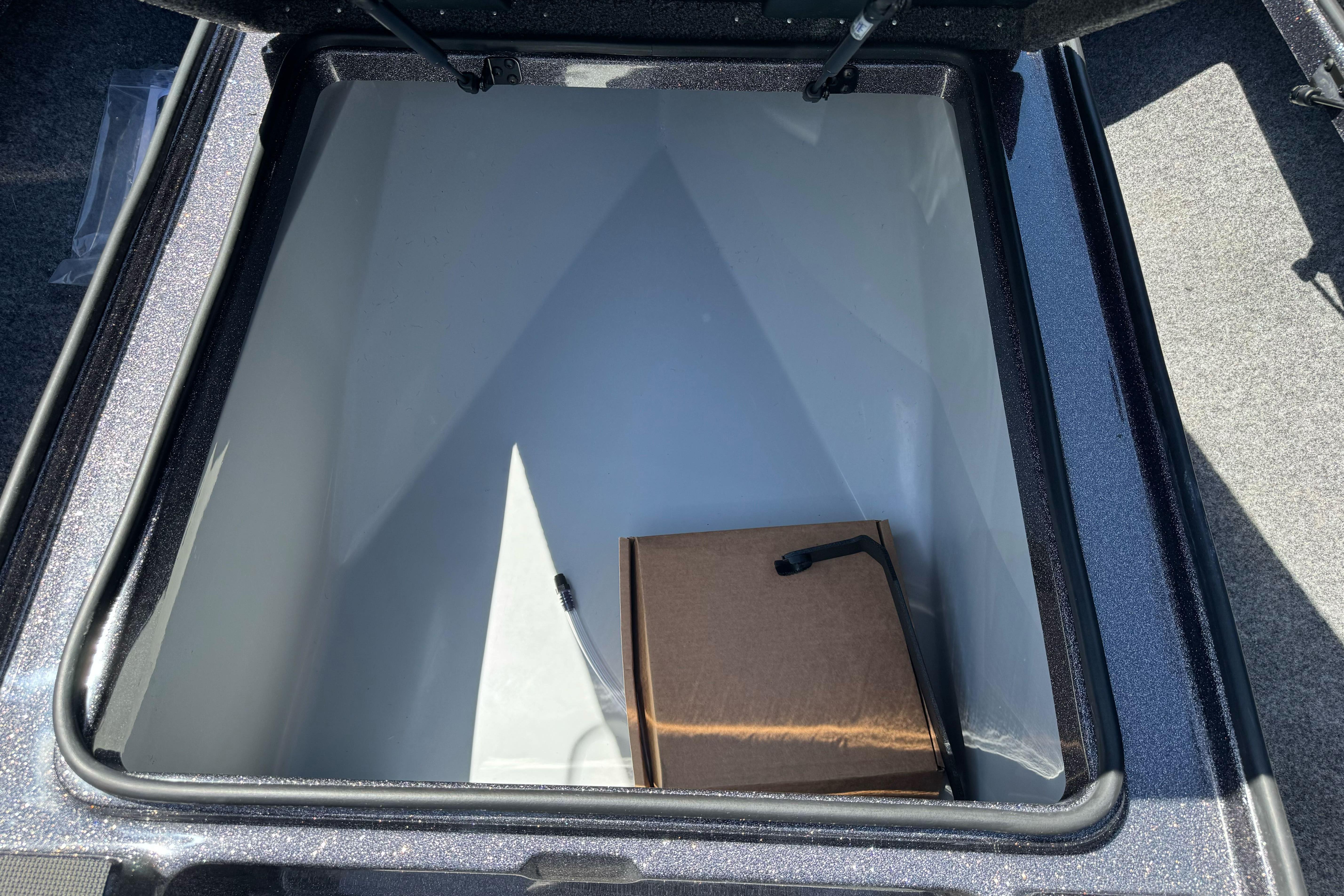 Open storage compartment in 2026 Triton 18 TrX boat, featuring a cardboard box inside.