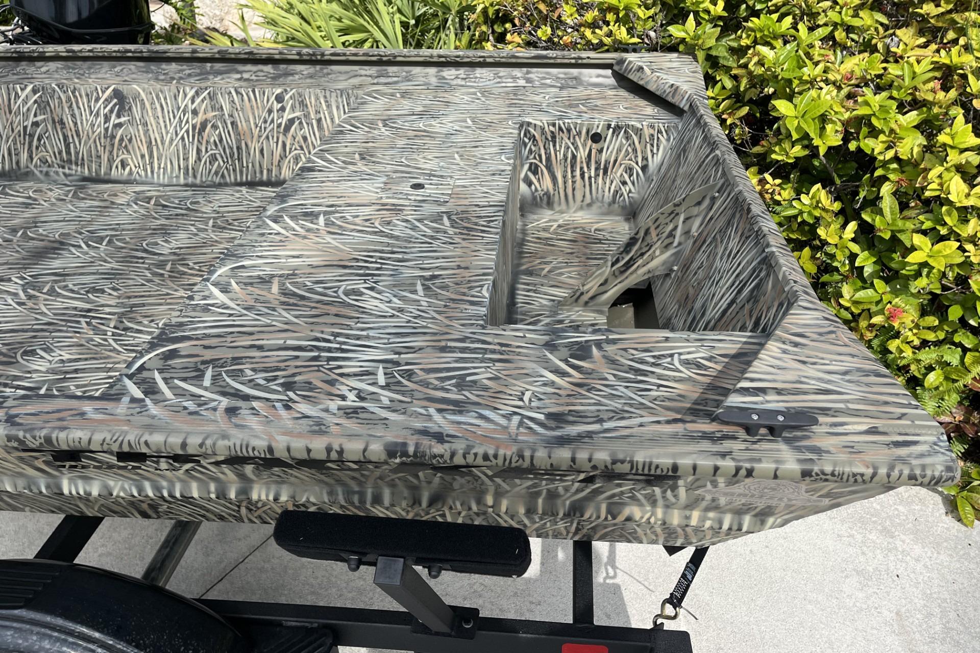 2025 Tracker Grizzly 1860 Utility boat with camouflage pattern, parked near greenery.