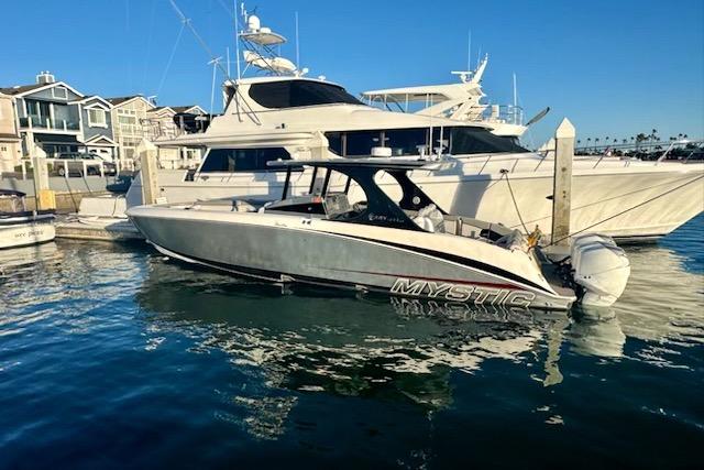 2016 Mystic M4200 boat docked in marina, clear blue sky, waterfront homes in background.