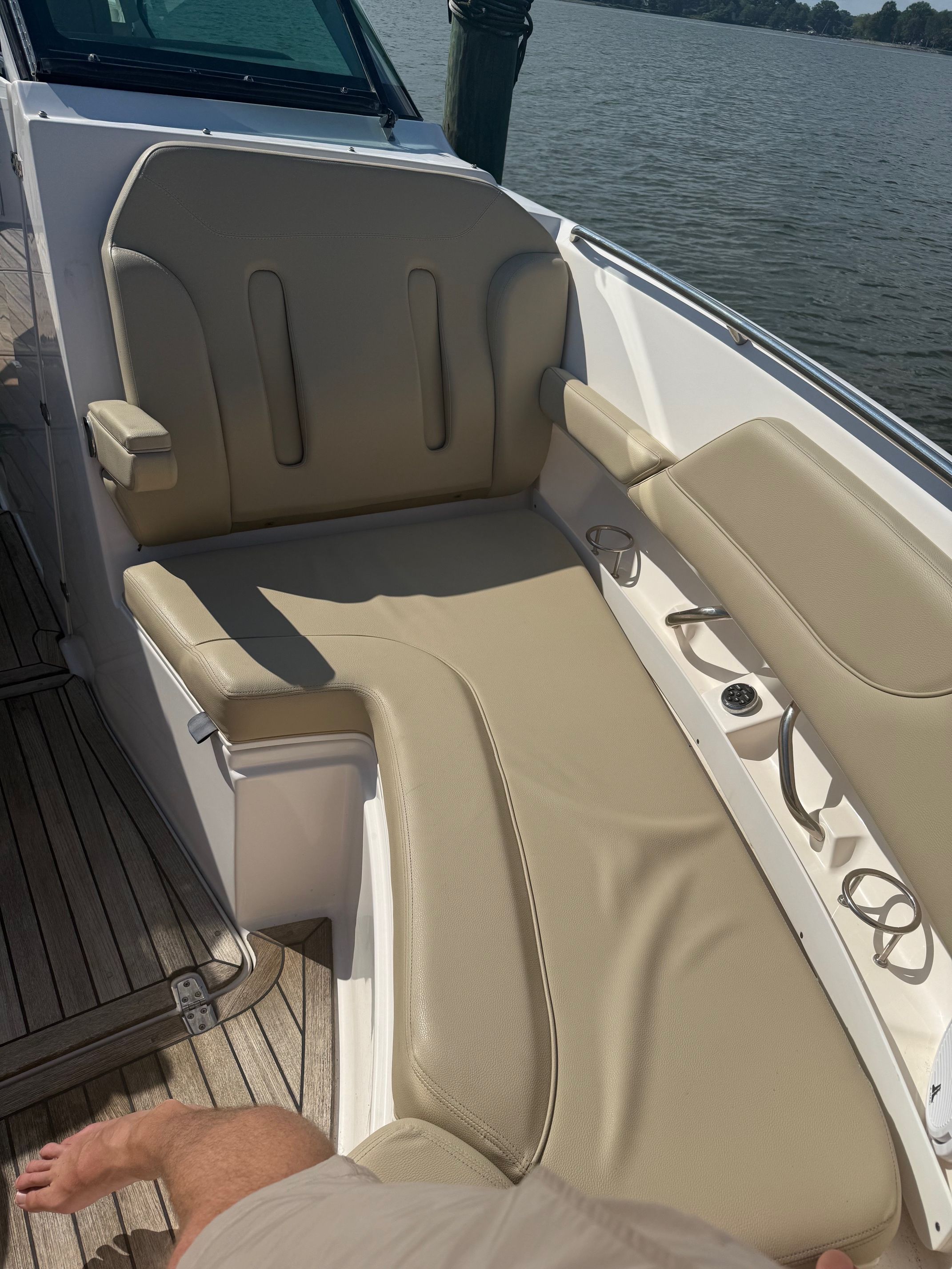 A beige leather sofa on a boat with wooden flooring, next to a body of water.