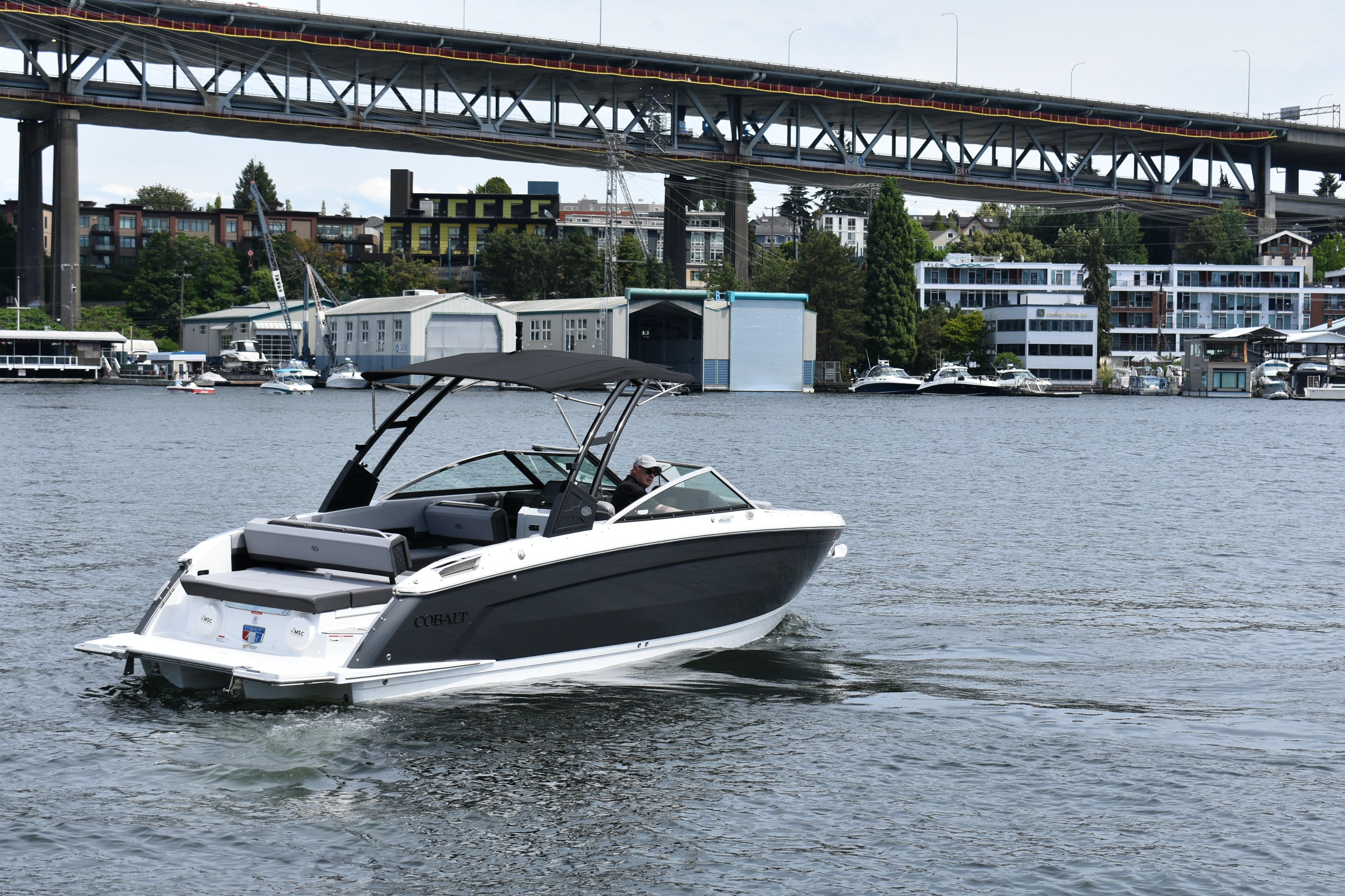 2023 Cobalt R8 boat cruising on a river with a bridge and buildings in the background.