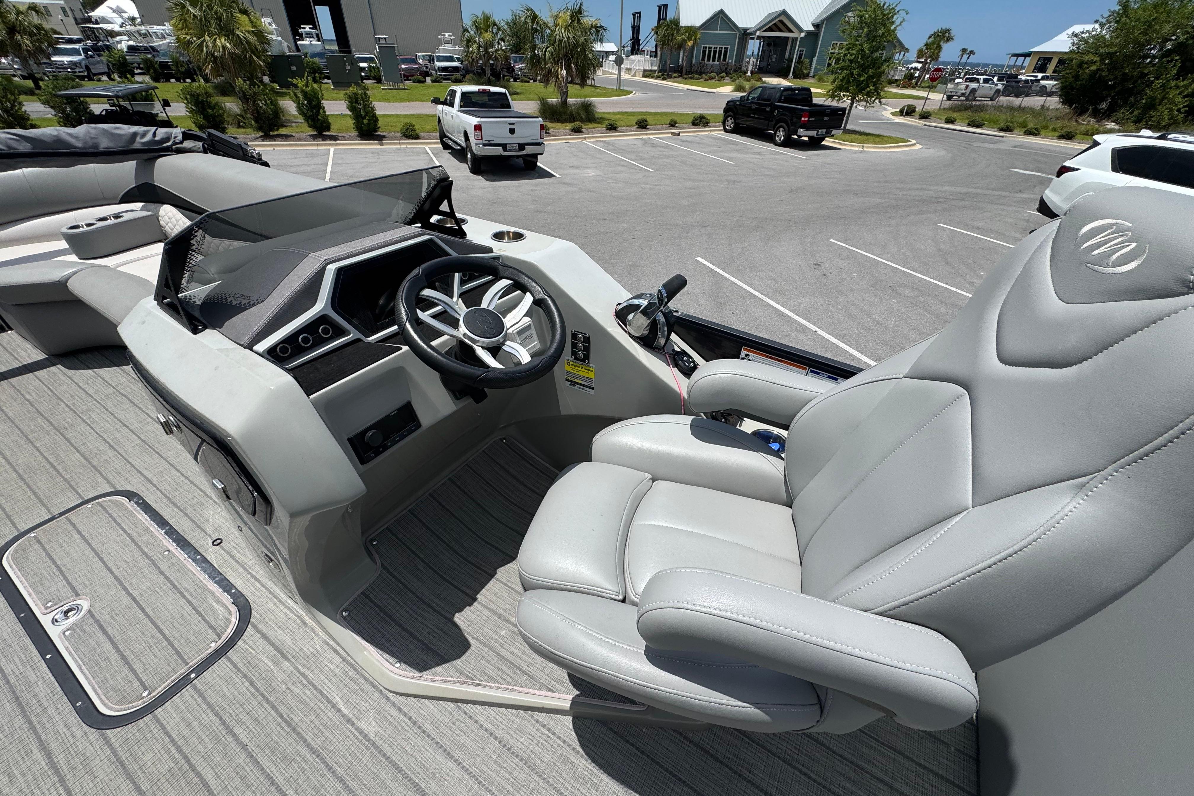 2022 Manitou 25 Encore boat interior with steering wheel and captain's chair in parking lot.