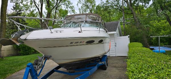 1999 Sea Ray 280 SS boat on trailer in driveway, surrounded by greenery.