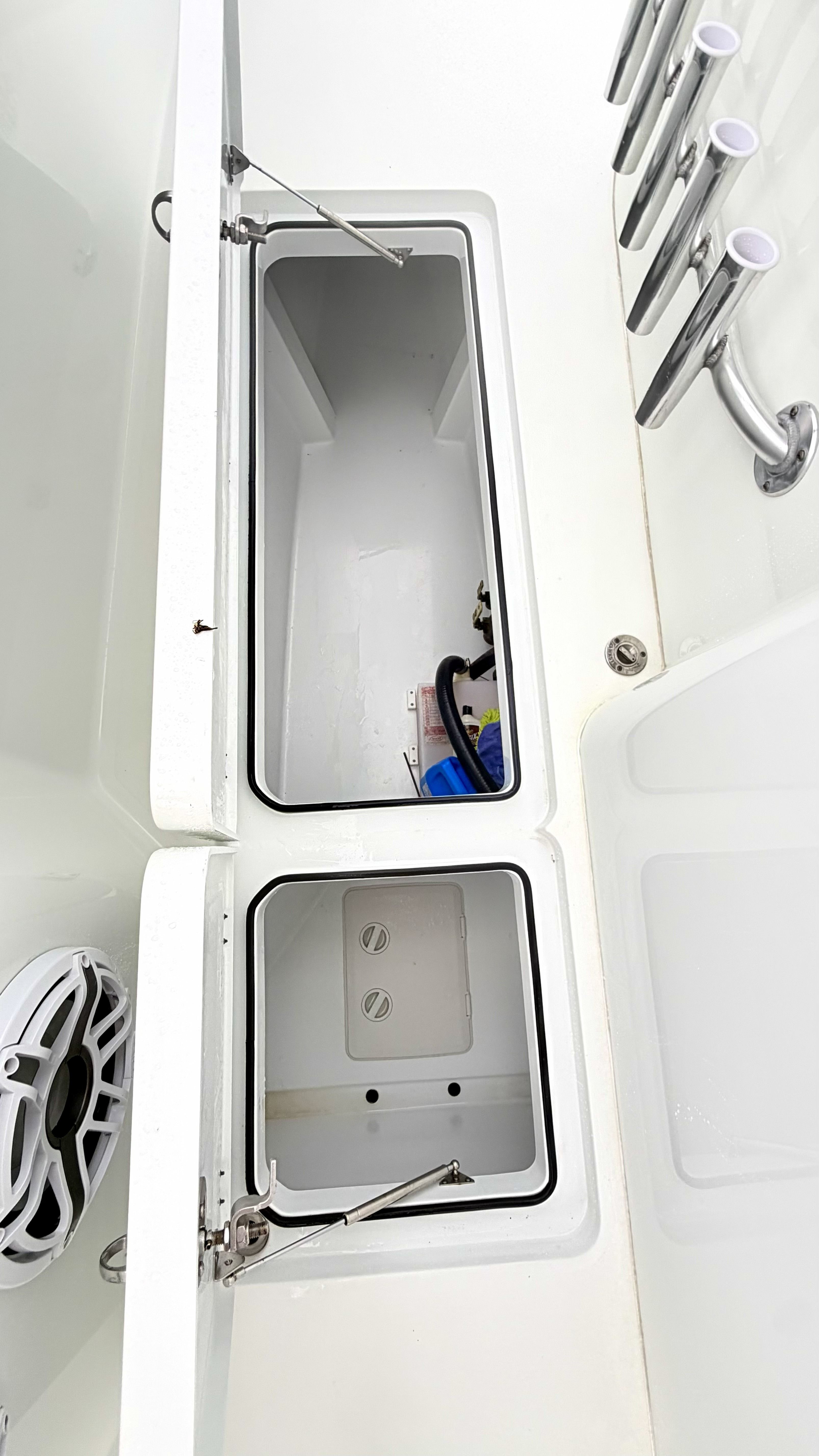 An open storage compartment on a boat with several rod holders beside it.