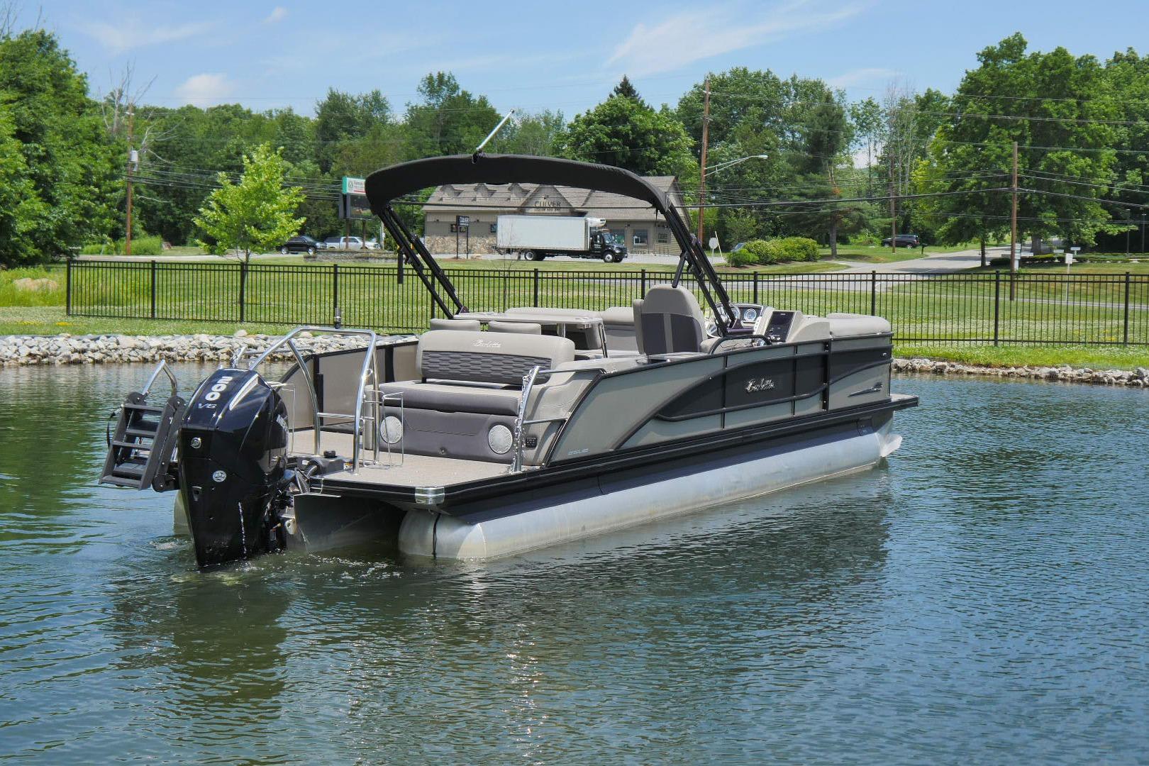 2023 Barletta CORSA 25UE pontoon boat on a calm lake, surrounded by greenery.