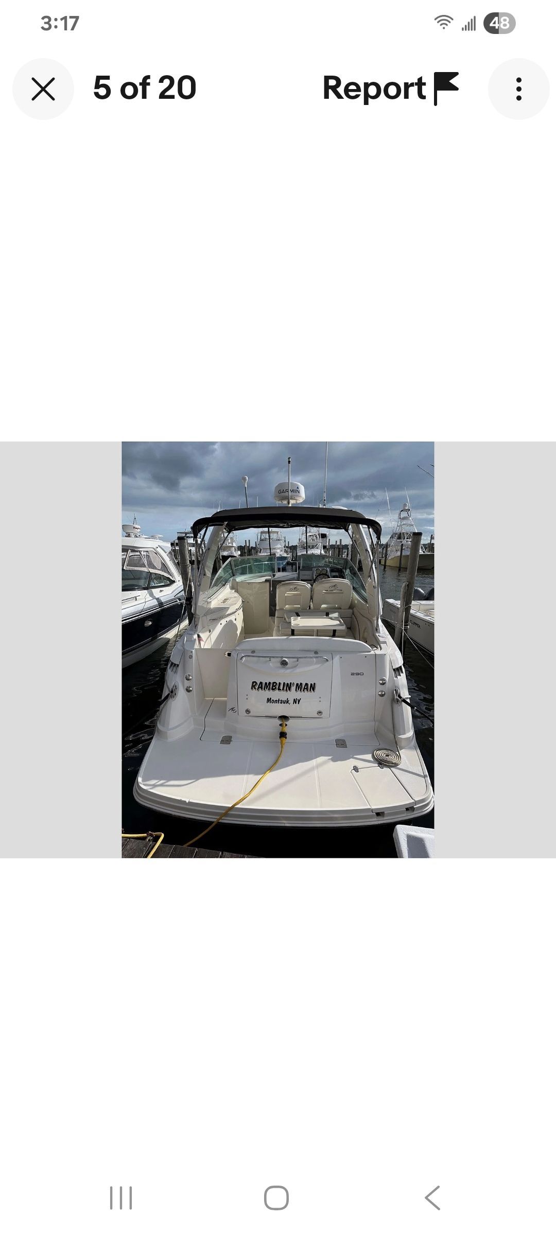 A white motorboat docked in a marina, featuring seating and an open cockpit.