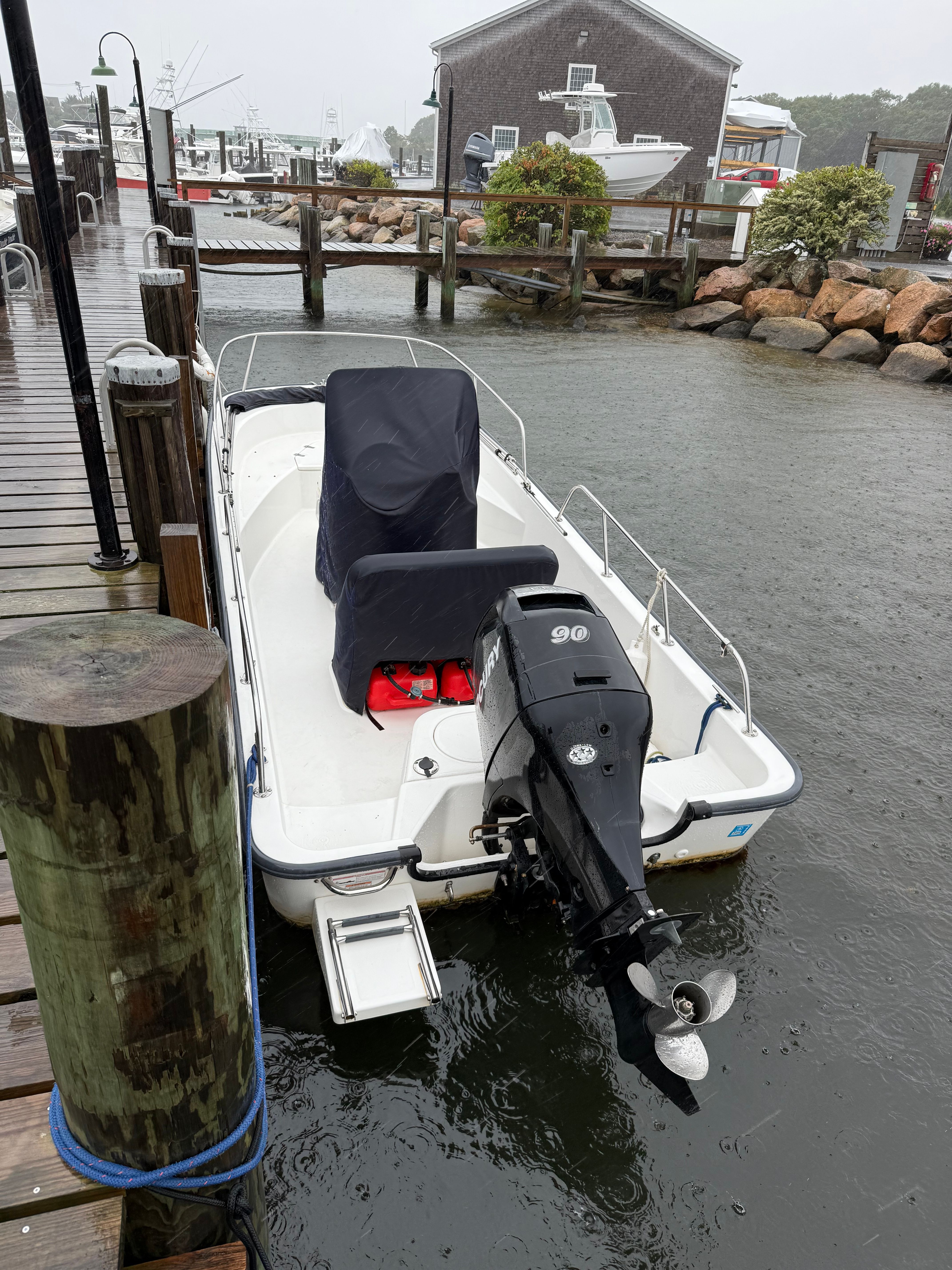 A 2011 Boston Whaler 170 Montauk docked on a rainy day, with a covered console and outboard motor.