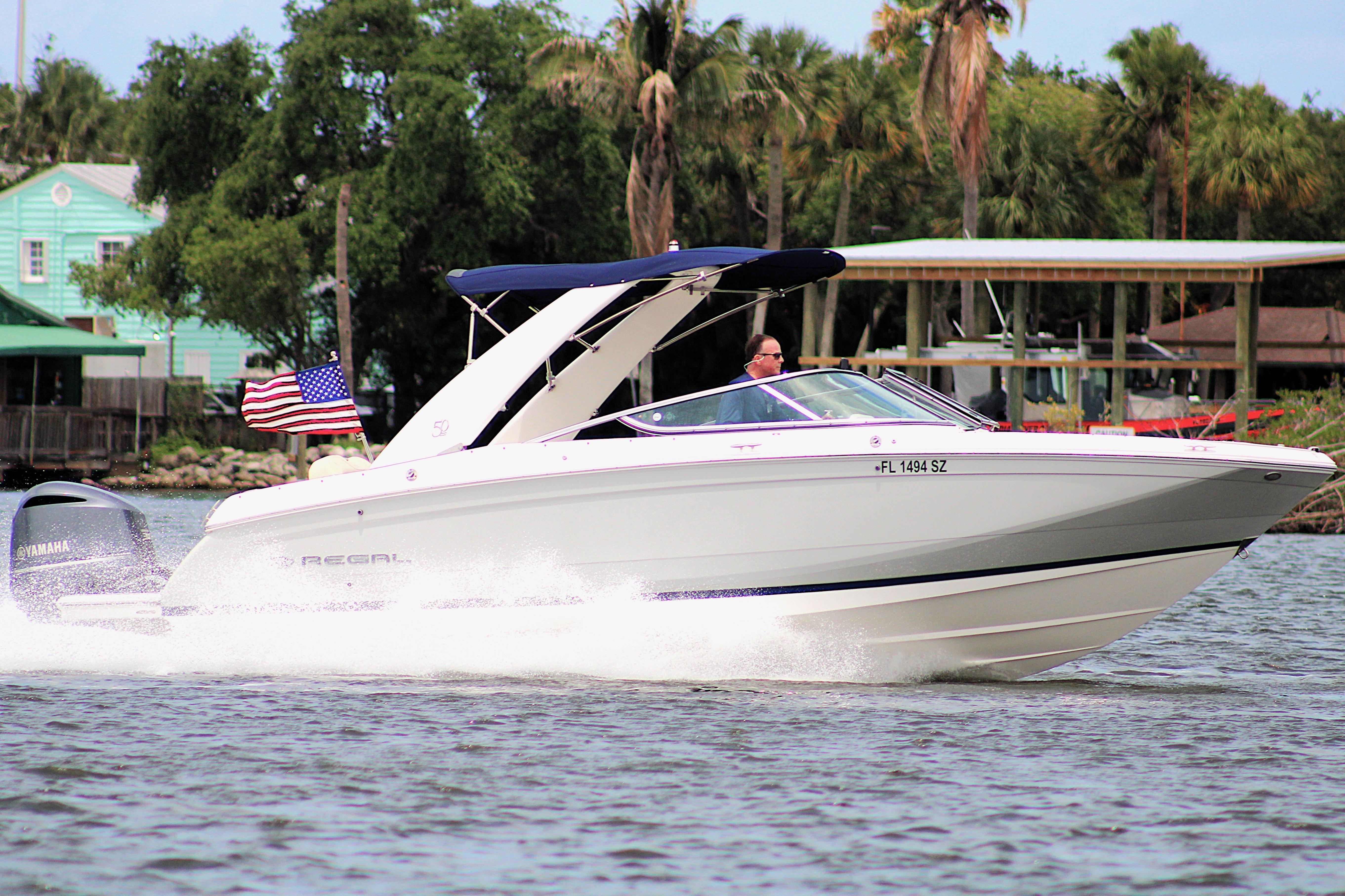 2021 Regal 26 OBX boat cruising on water with American flag, lush greenery in background.