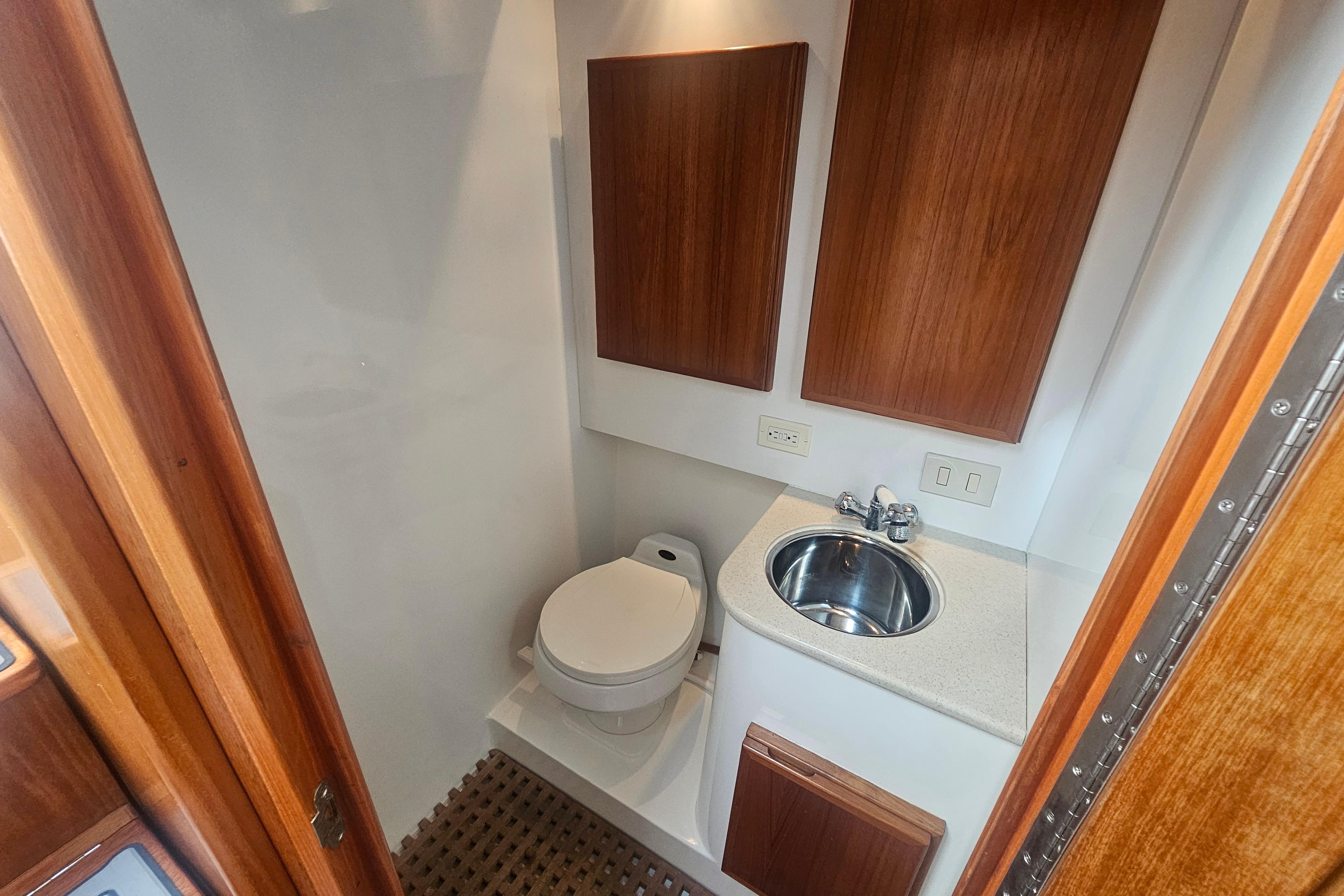2003 Topaz 32 Express boat bathroom with toilet, sink, and wooden cabinetry.