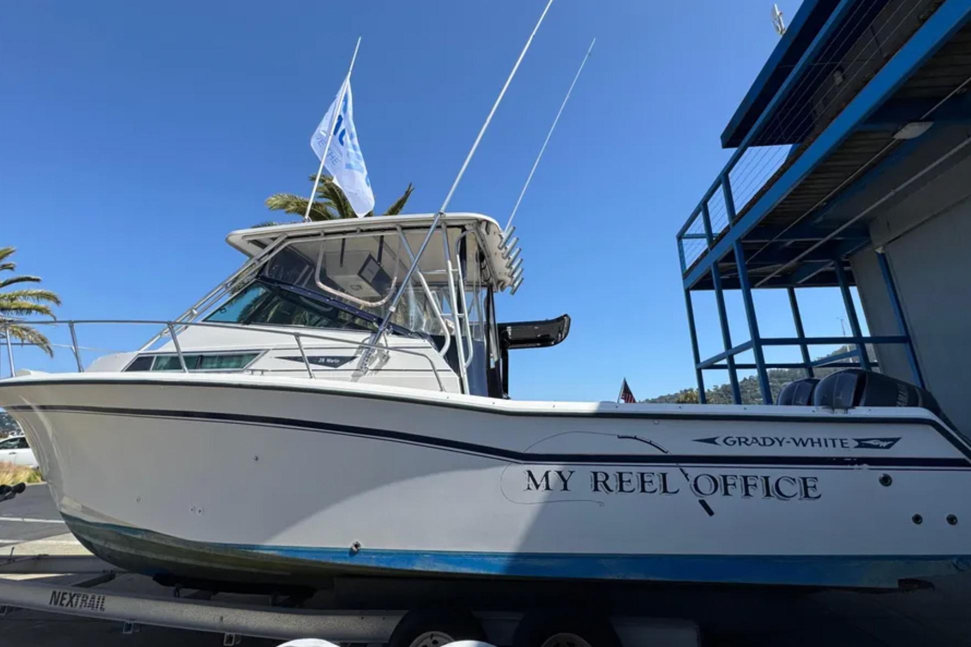 1990 Grady-White Marlin 280 boat named "My Reel Office" on trailer, blue sky background.