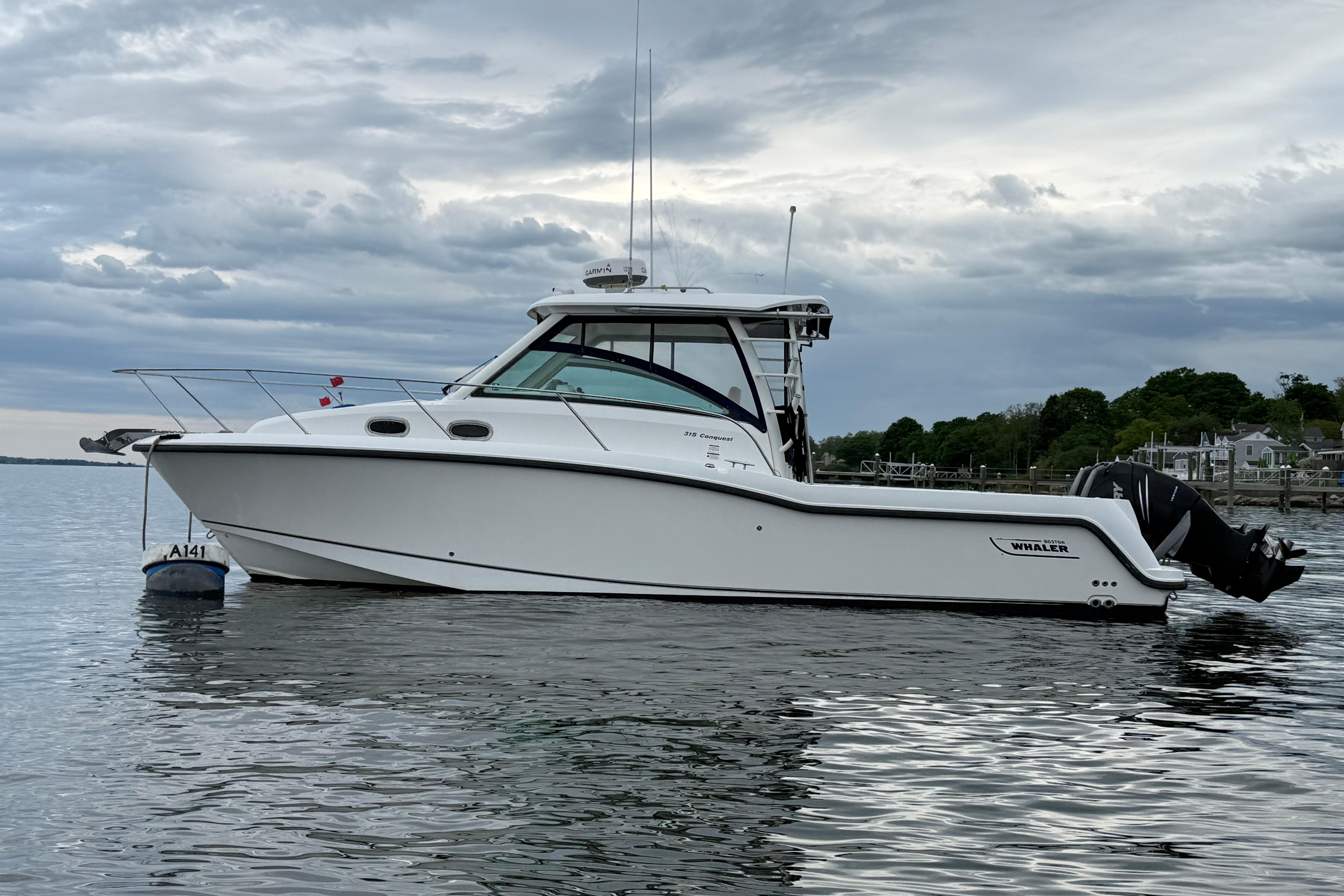 2013 Boston Whaler 315 Conquest boat on calm water under cloudy sky.