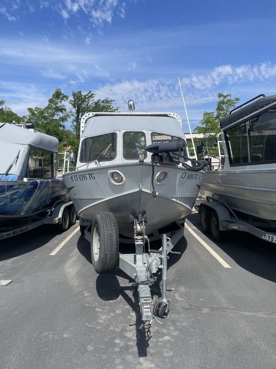 A silver open bow boat on a trailer in a parking lot.