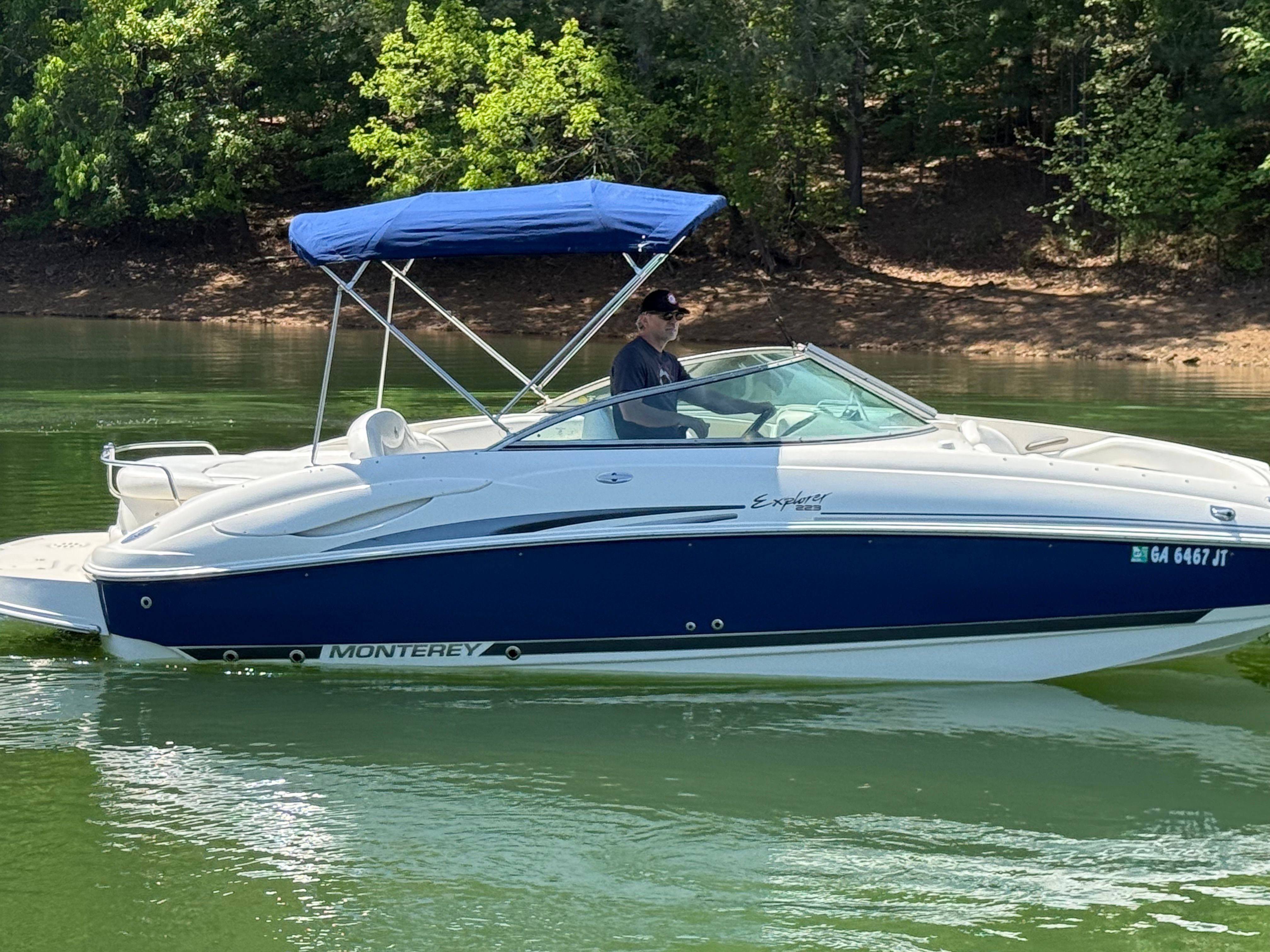 A white and blue 2005 Monterey 223 Explorer Sport boat cruising on a calm lake.