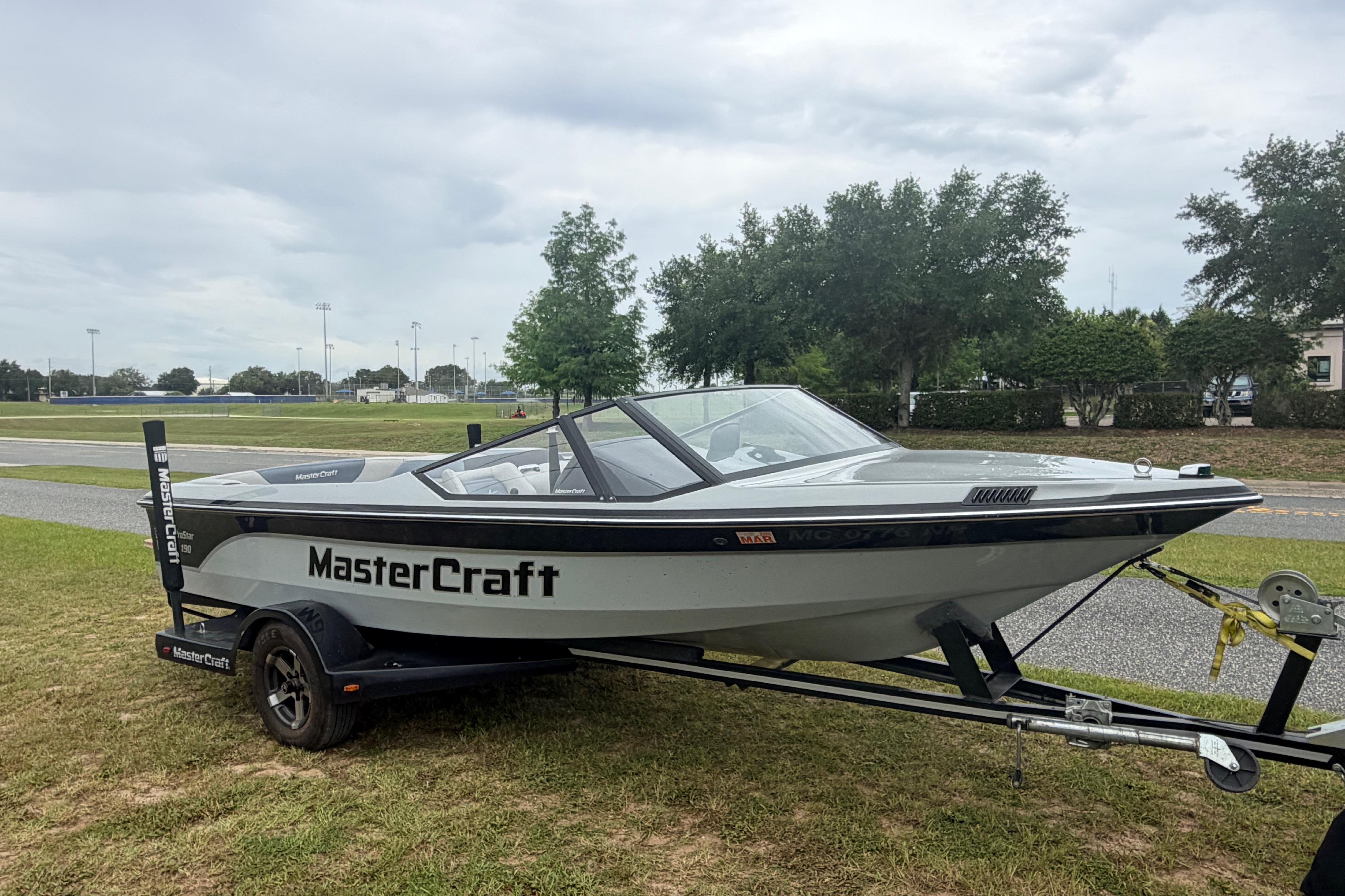1989 MasterCraft ProStar 190 boat on trailer, parked on grass, overcast sky.