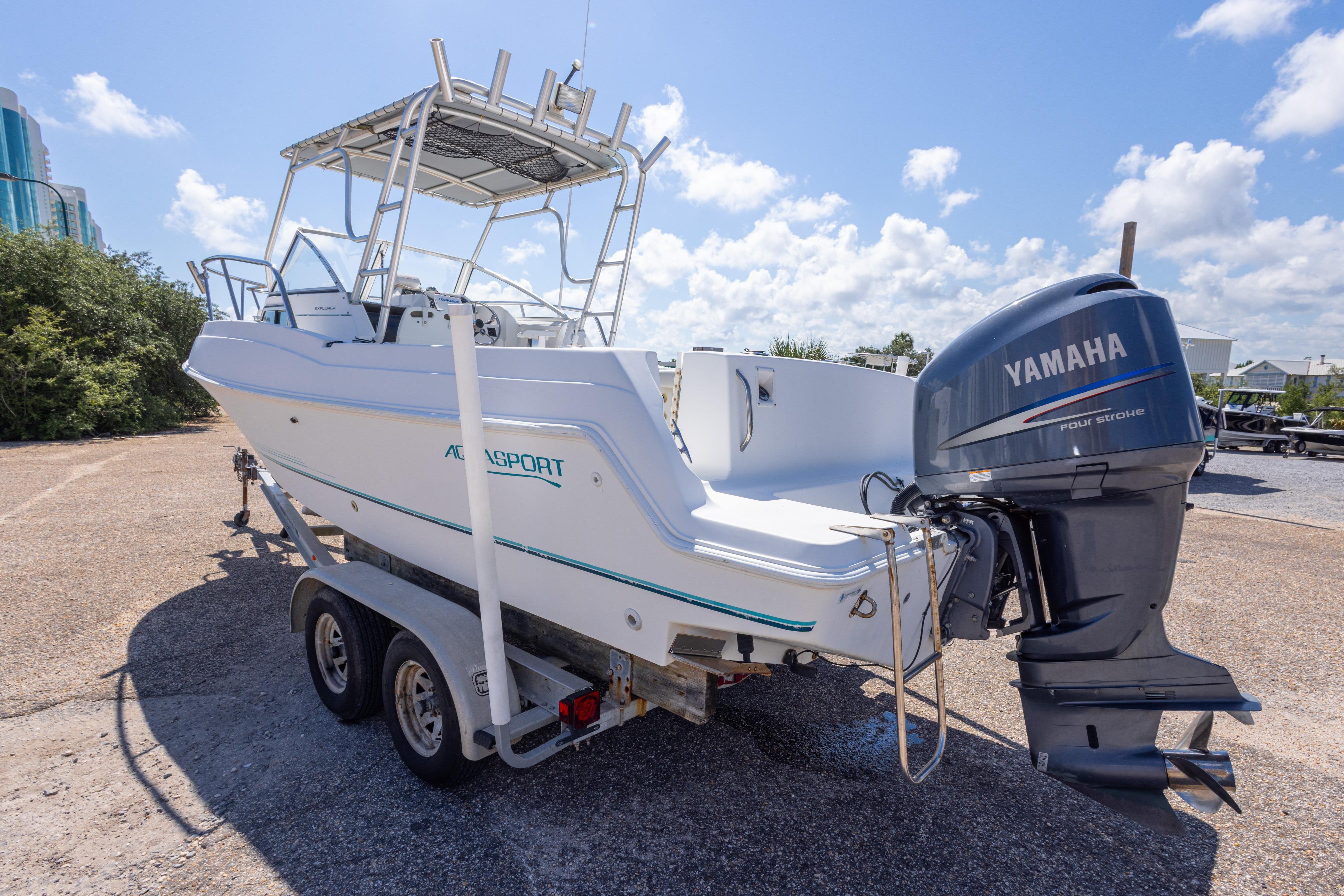 1999 Aquasport 225 Explorer boat with Yamaha outboard motor on a trailer, parked outdoors.