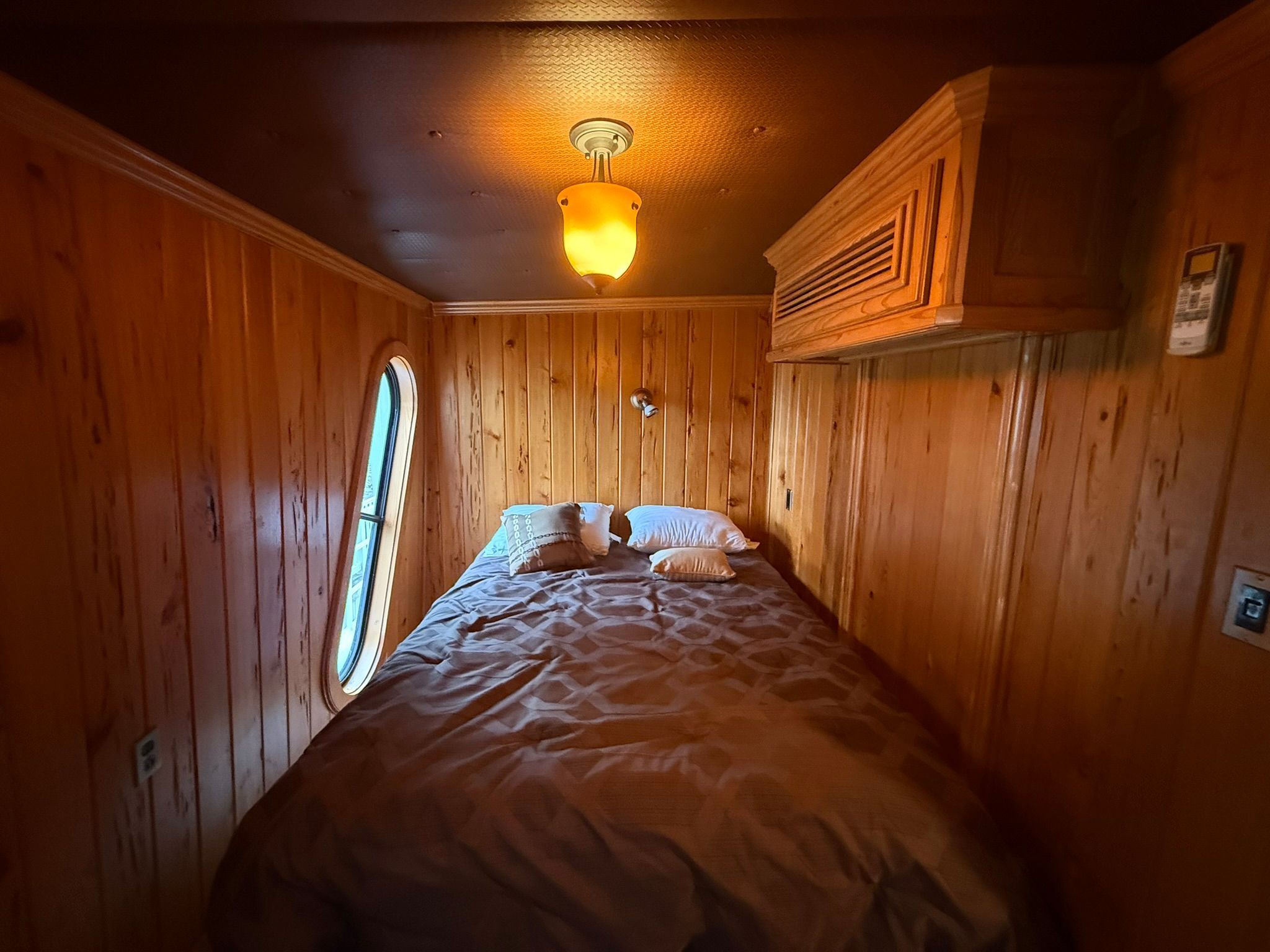 A cozy bedroom with wood paneling and an oval window.