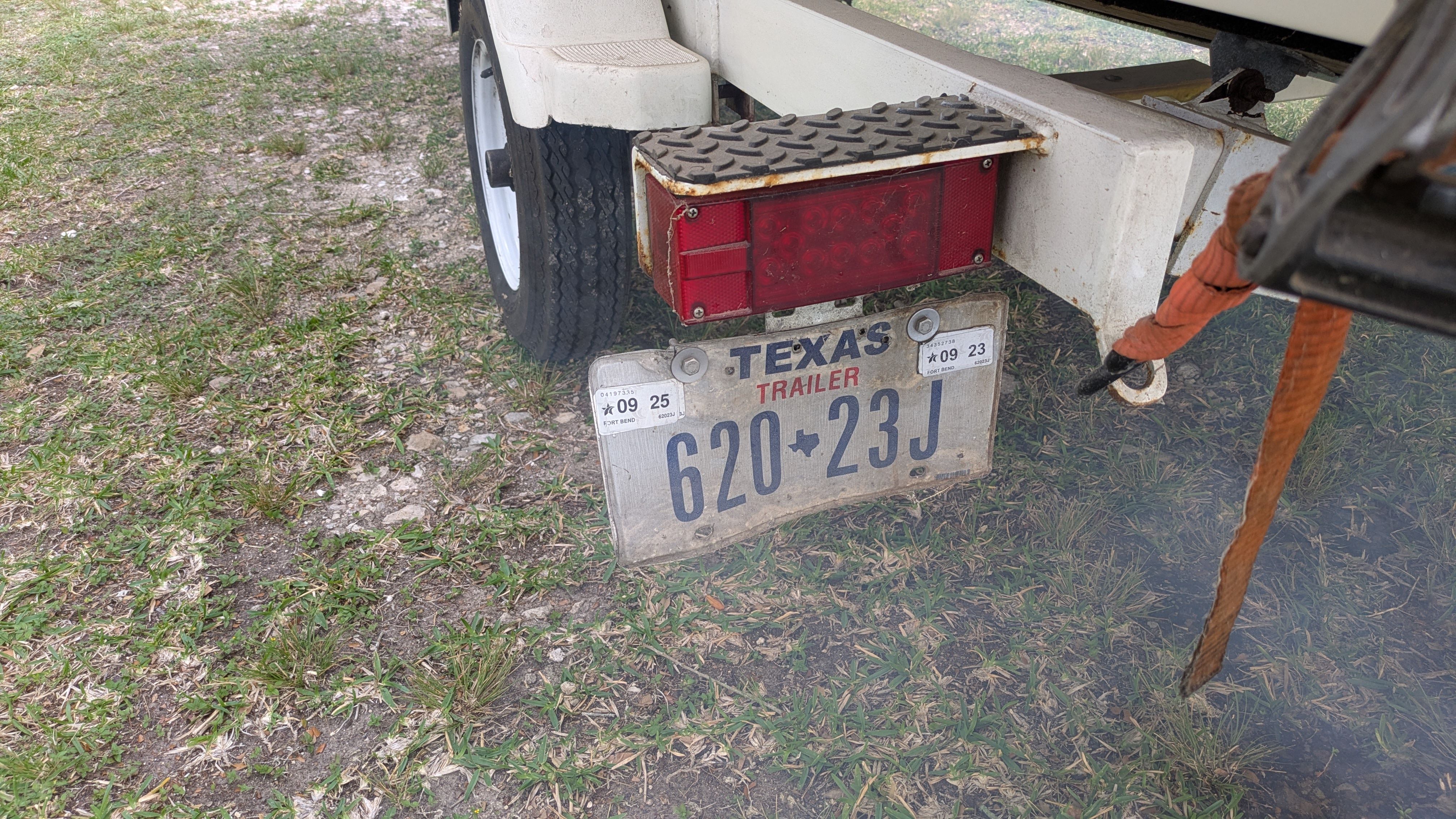 A boat trailer with a Texas license plate is parked on grass.