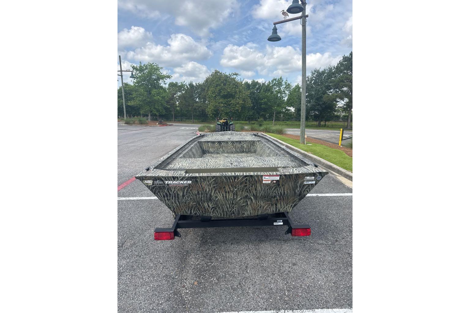 2026 Tracker Grizzly 1648 Utility boat in parking lot, camo design, under cloudy sky.