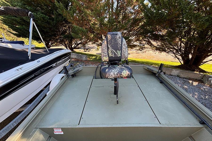 2022 Lowe Roughneck 1660 boat with camo seat, parked outdoors near trees.