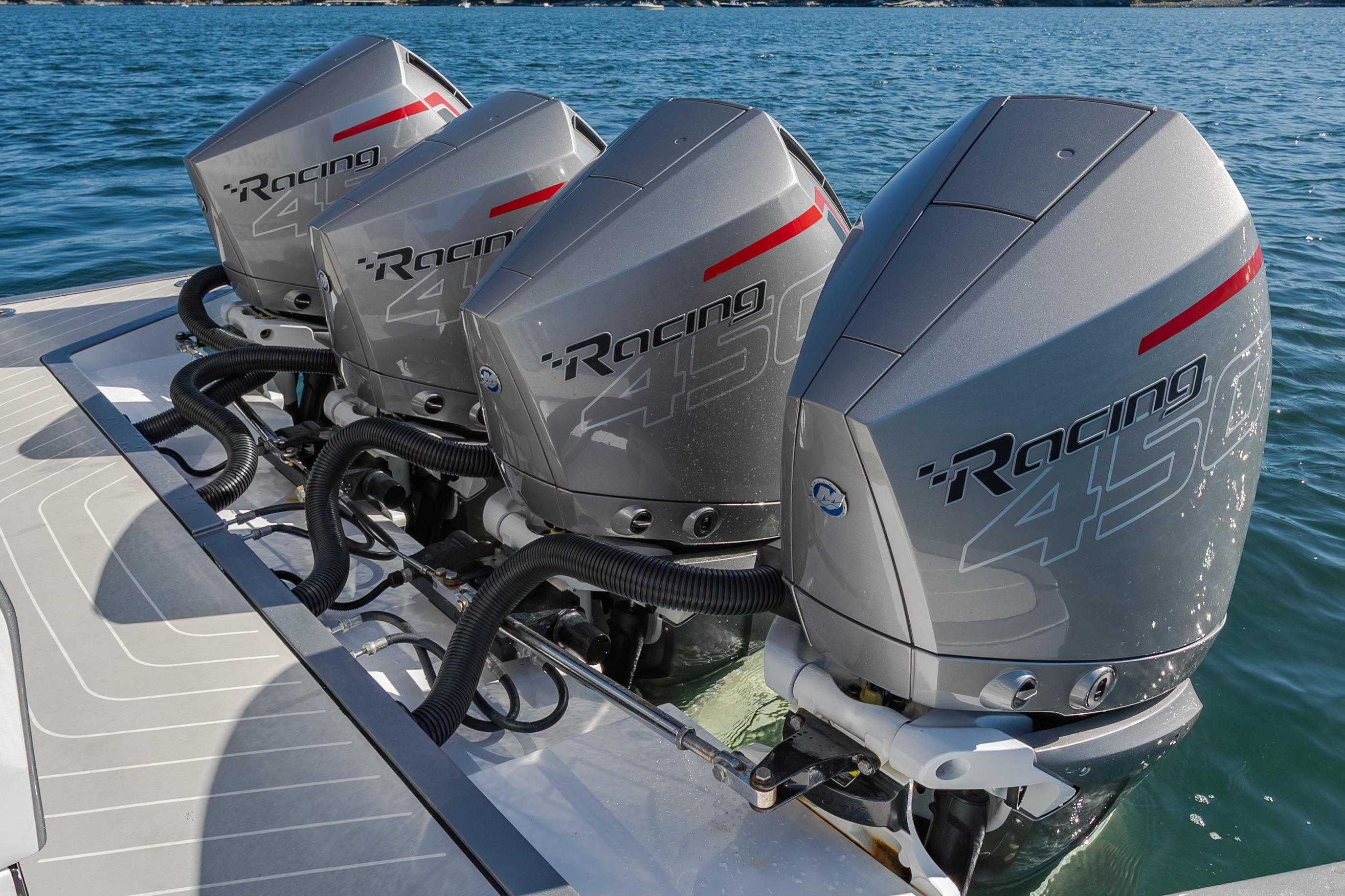 Four powerful outboard engines on a boat in calm water.