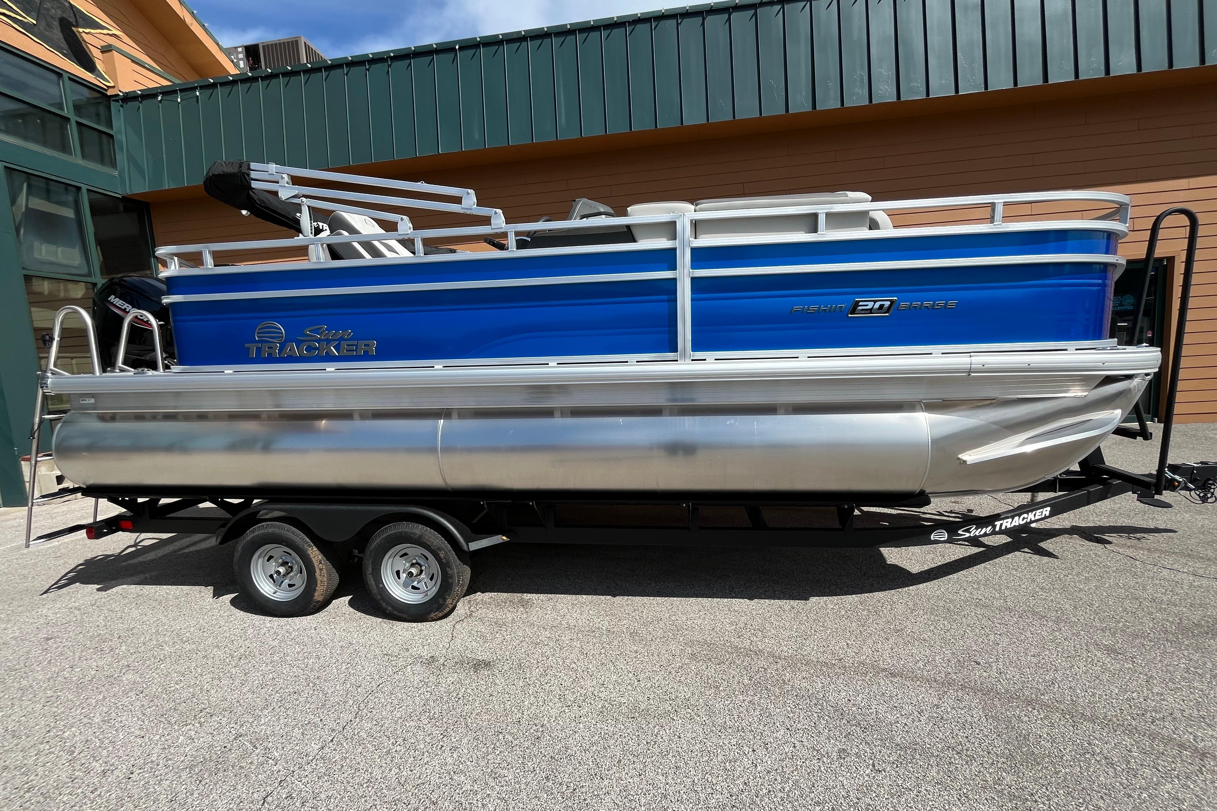 2026 Sun Tracker Fishin' Barge 20 DLX pontoon boat on trailer, blue and silver design.