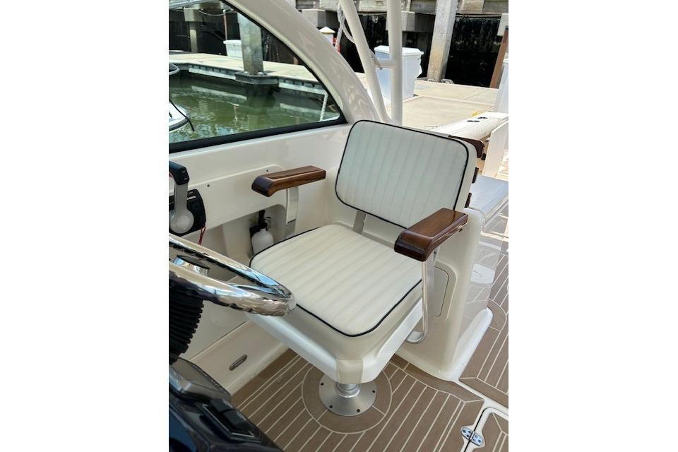 Captain's chair on 2013 Pursuit DC 265 Dual Console boat, featuring white upholstery and wooden armrests.