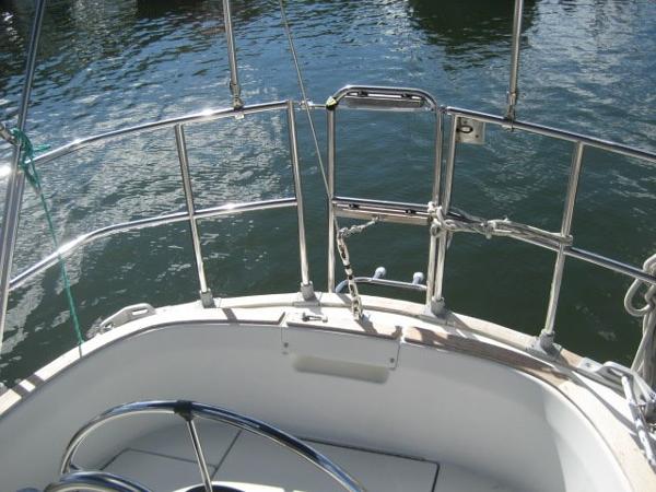 View from the stern of a boat with stainless steel railing and steering wheel, surrounded by water.