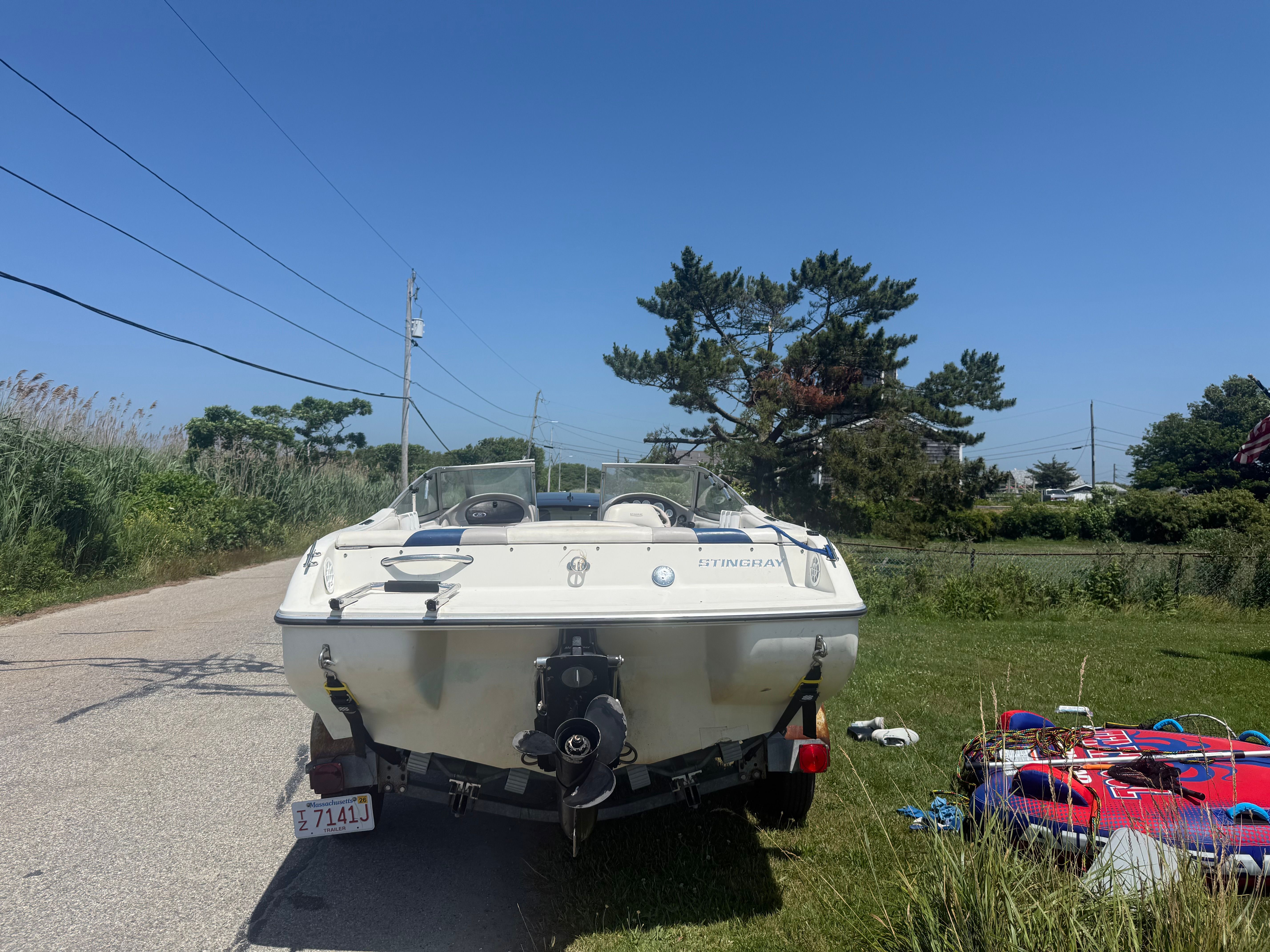 A white boat, a 2003 Stingray 180 LS/LX, is on a trailer beside a road.