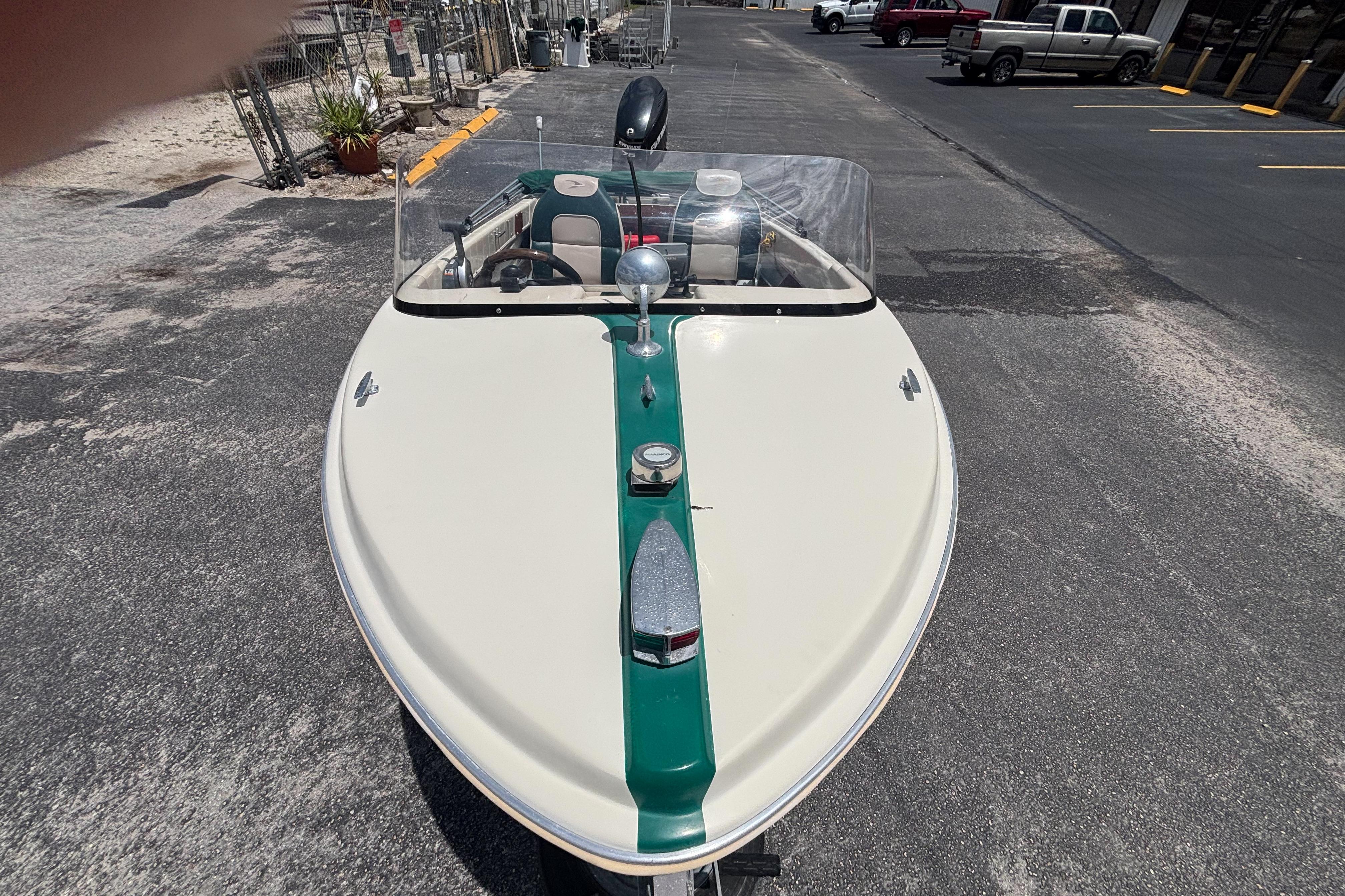 1966 Mohawk 15 boat with green stripe, parked on asphalt, featuring windshield and steering wheel.