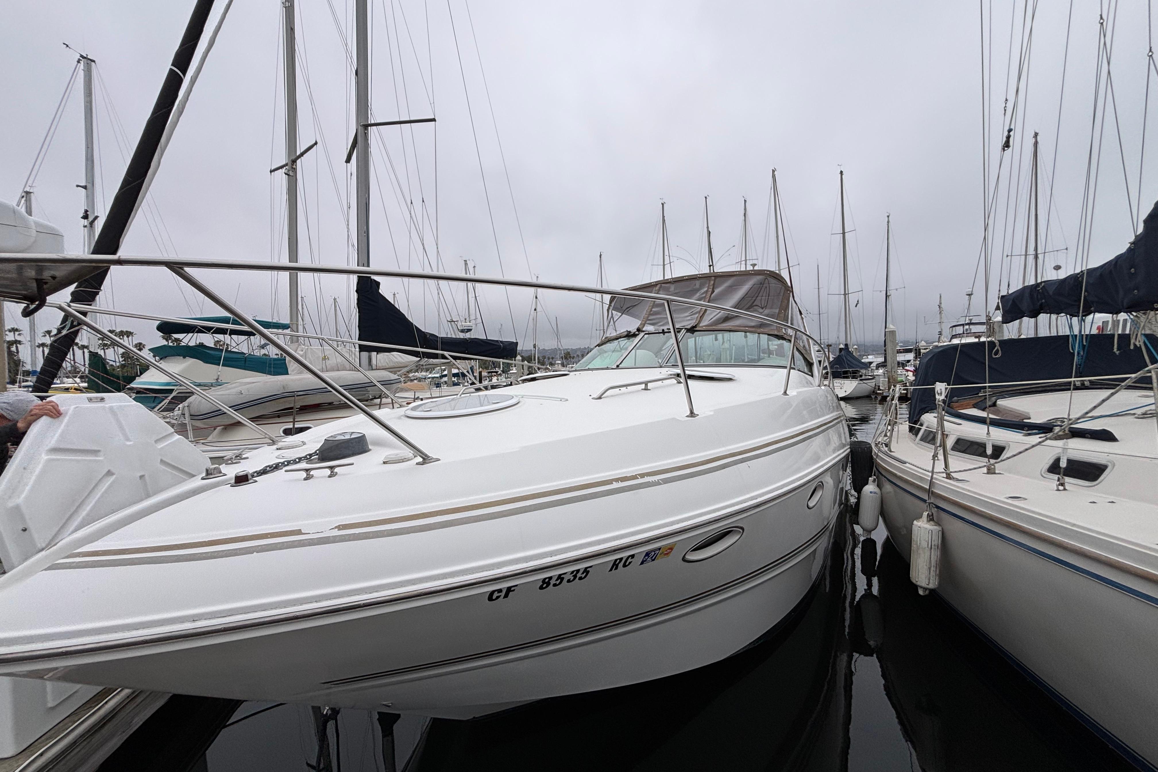 2004 Larson 310 boat docked among sailboats in a marina on a cloudy day.