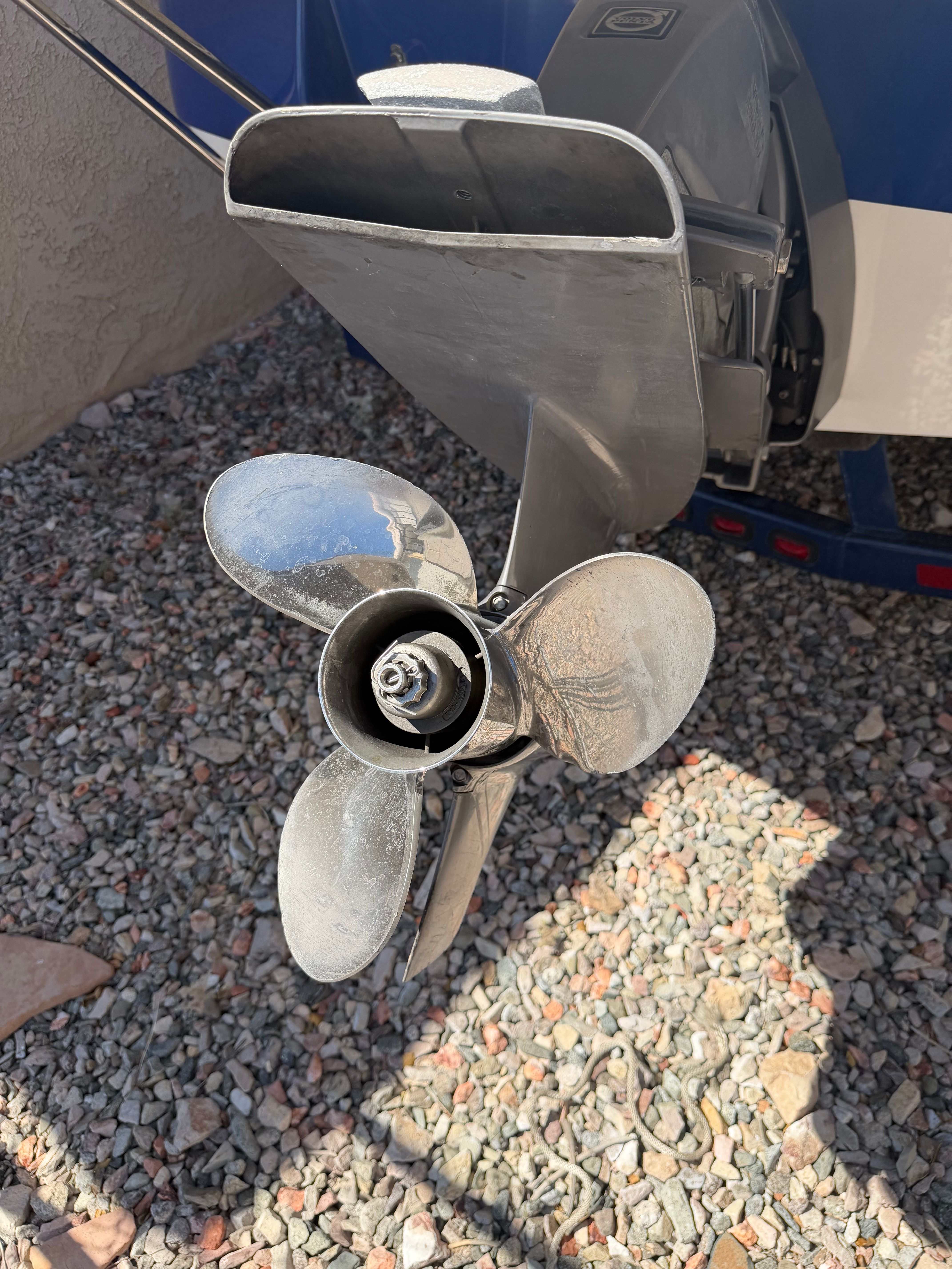 Close-up of a boat propeller on a gravel surface.