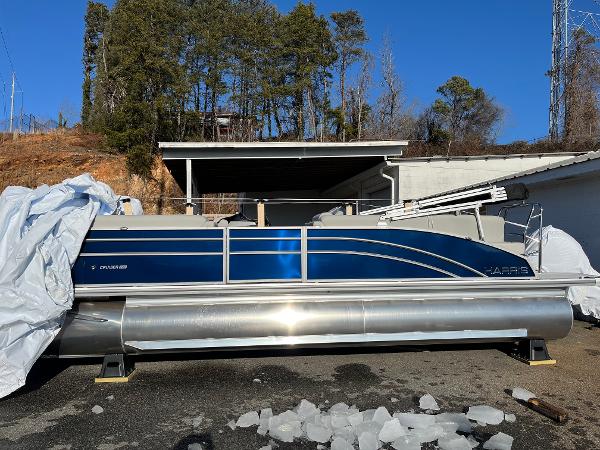2025 Harris Cruiser 230 pontoon boat in a driveway, partially covered, with trees in the background.