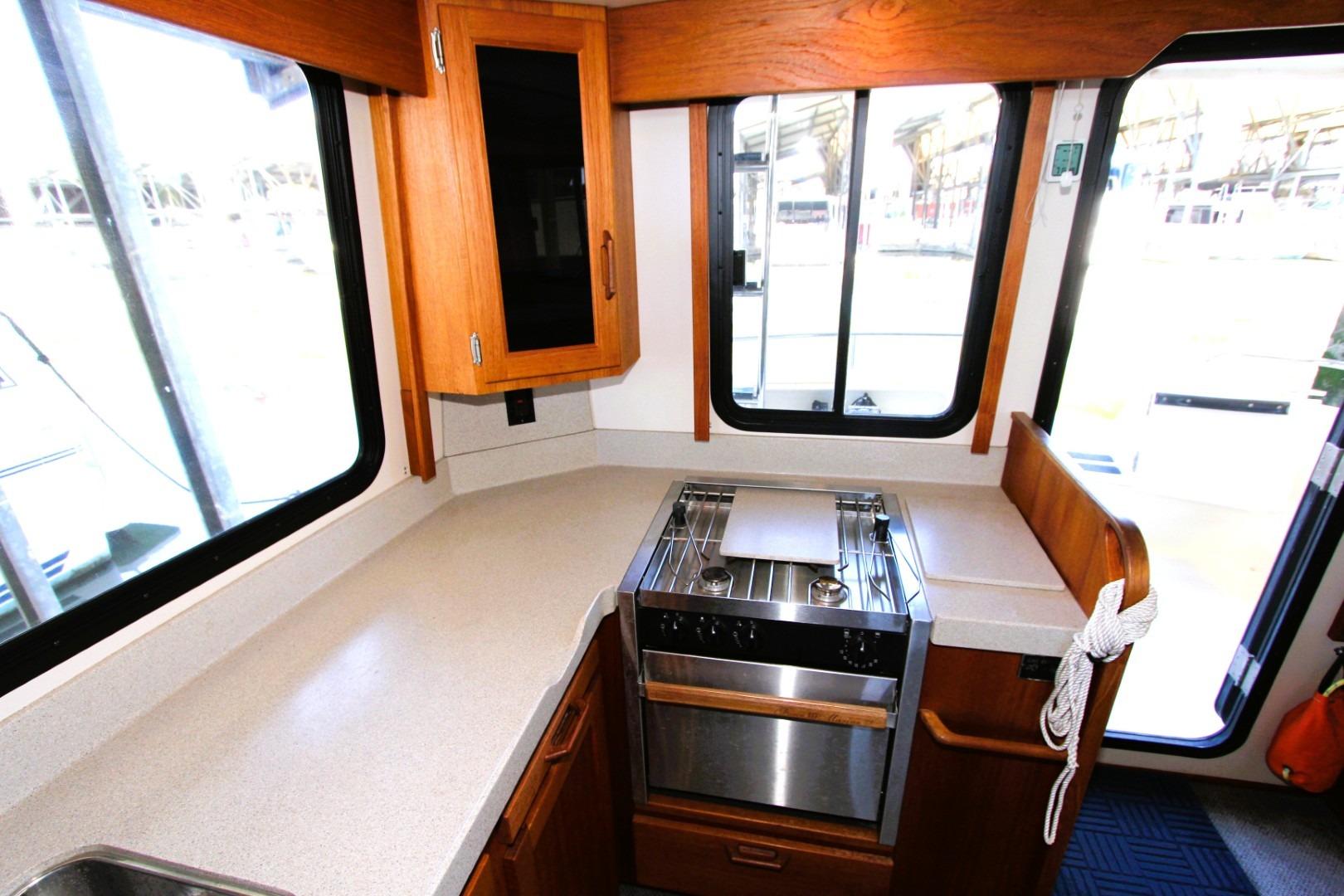 2002 Nordic Tug 37 interior kitchen with stove, wooden cabinets, and large windows.