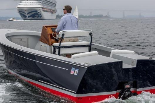 2024 C.W. Hood 26E Electric Runabout cruising on open water with a large ship in the background.