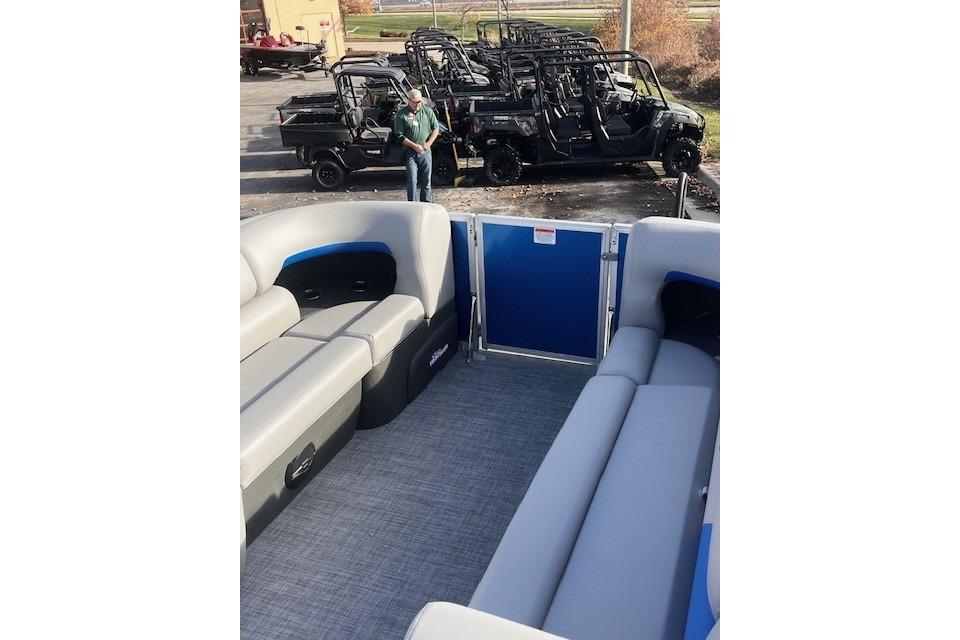 2026 Sun Tracker Party Barge 20 DLX interior with gray seating, parked utility vehicles in background.