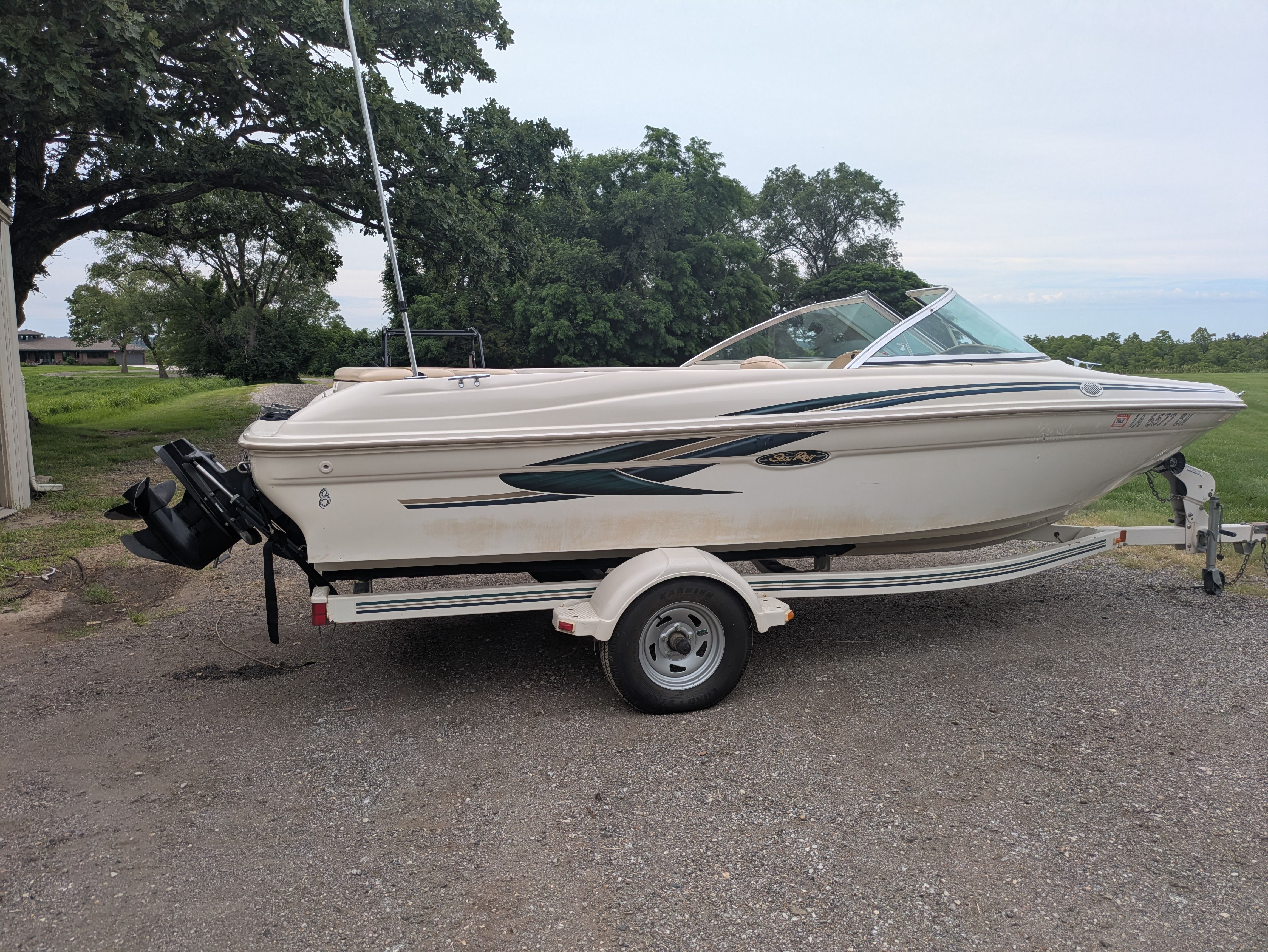 A Sea Ray 185 Bow Rider boat on a trailer, surrounded by trees and grass.