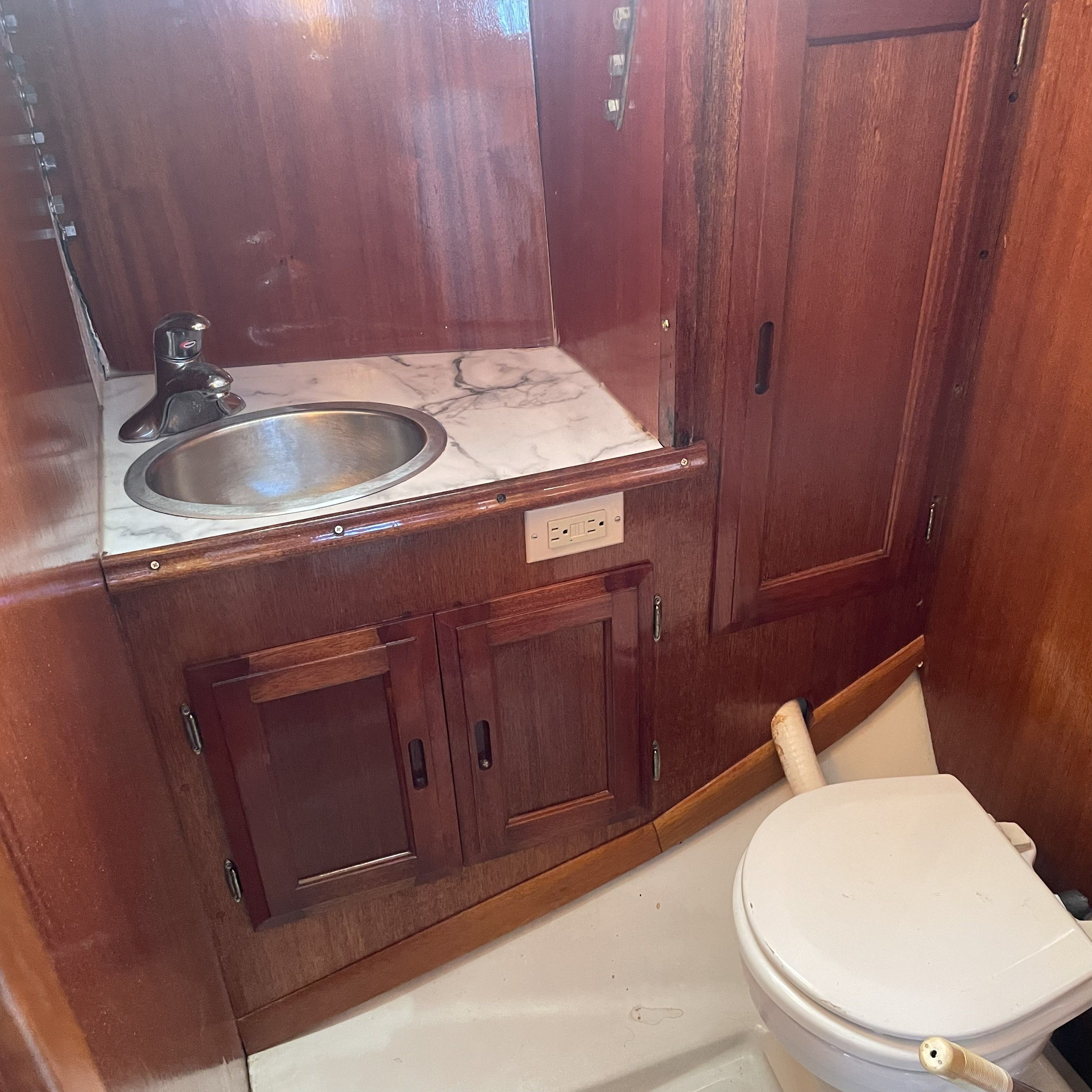 Interior view of a boat bathroom with wood paneling, sink, and toilet.