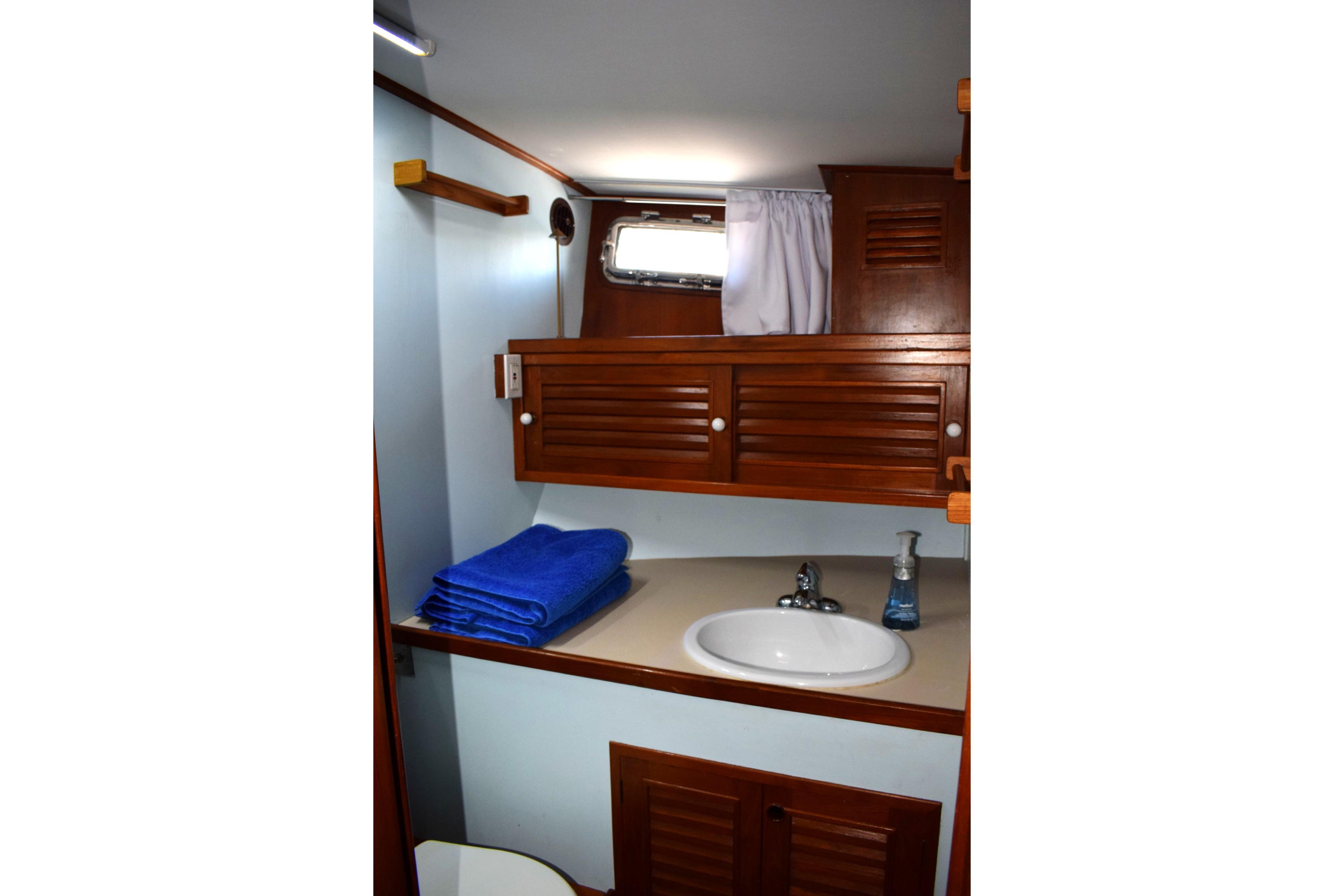 1980 Cheoy Lee 52 Motorsailer bathroom with wooden cabinets, sink, and blue towels.