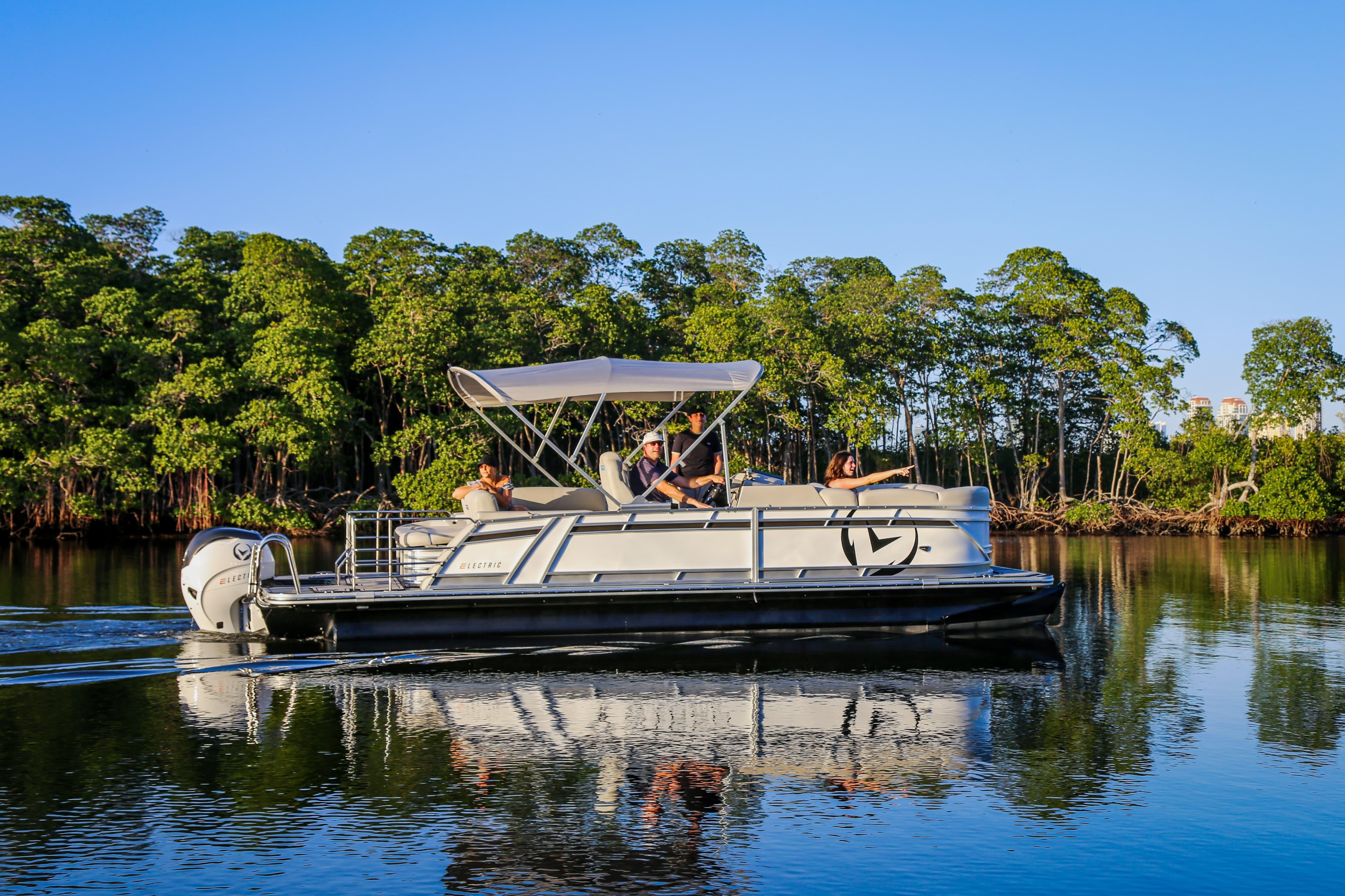 2025 Vision Marine Technologies V24 electric boat cruising on calm water near lush greenery.