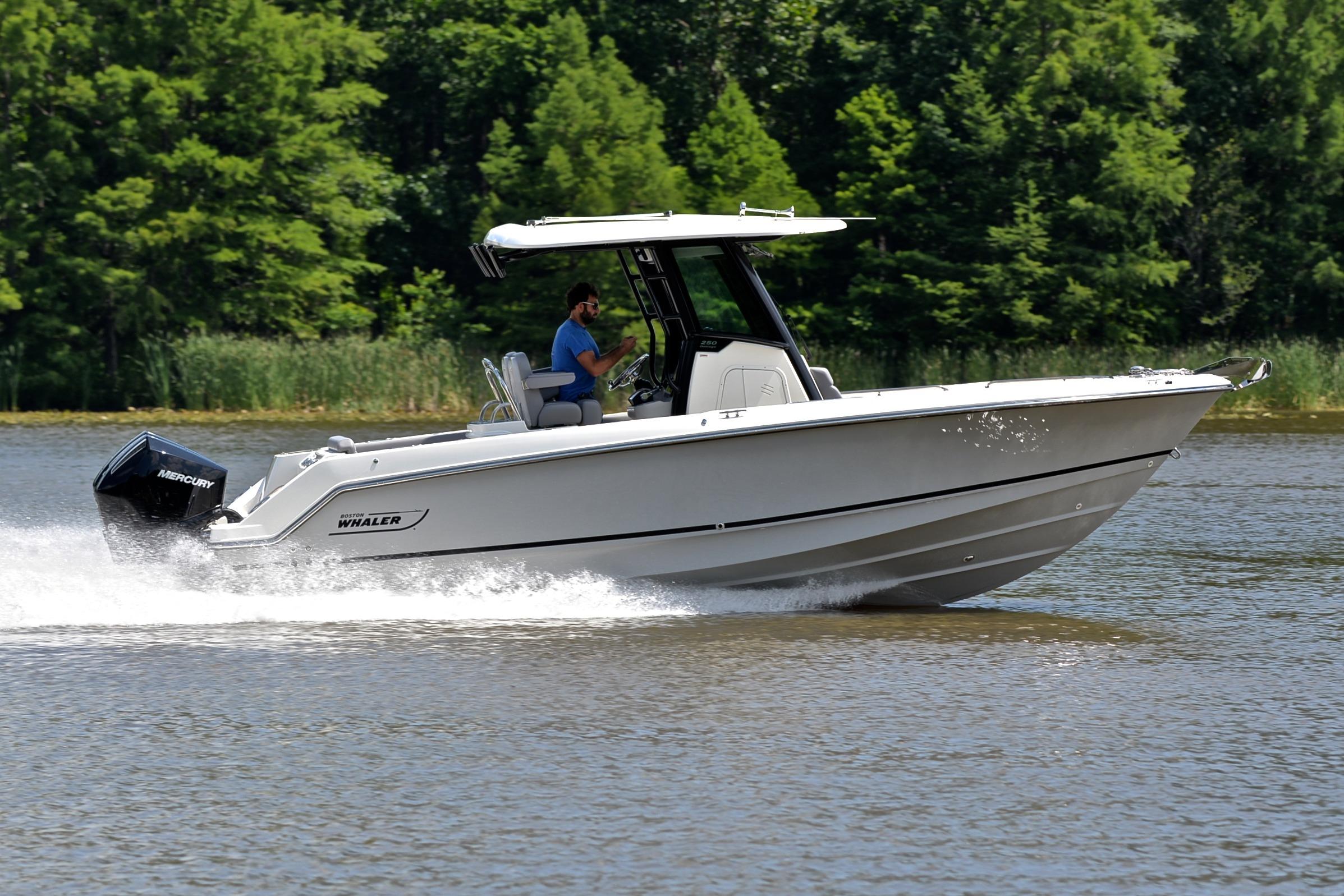 2024 Boston Whaler 250 Outrage cruising on a lake with lush green trees in the background.