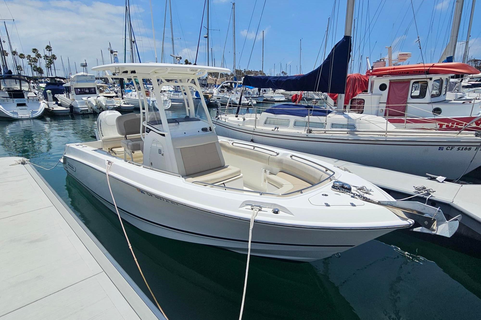 2017 Boston Whaler 230 Outrage docked at a marina, surrounded by sailboats.