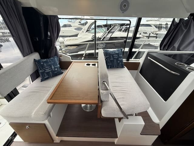 Interior of the Jeanneau NC 1095 featuring a table and benches, surrounded by windows overlooking other boats.
