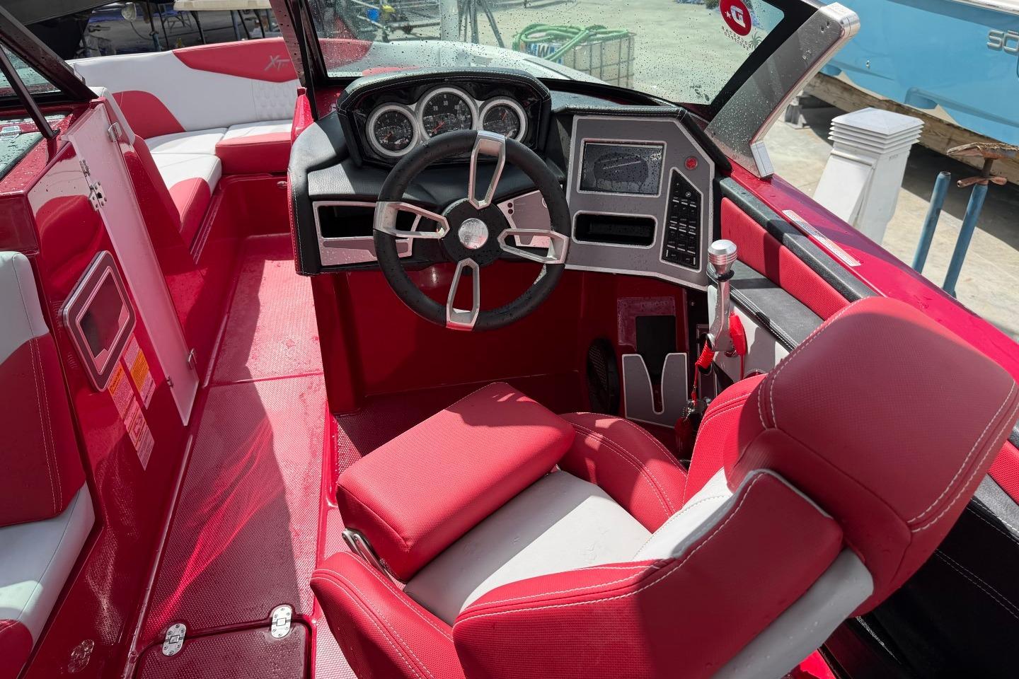 2023 MasterCraft X24 boat interior with red and white seating, modern dashboard, and steering wheel.