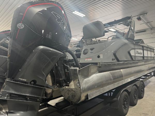 2025 Manitou LX pontoon boat with powerful outboard motor in a garage setting.