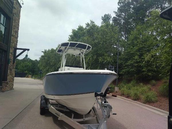 2023 Mako 214 CC boat on a trailer, parked outdoors near trees and a building.
